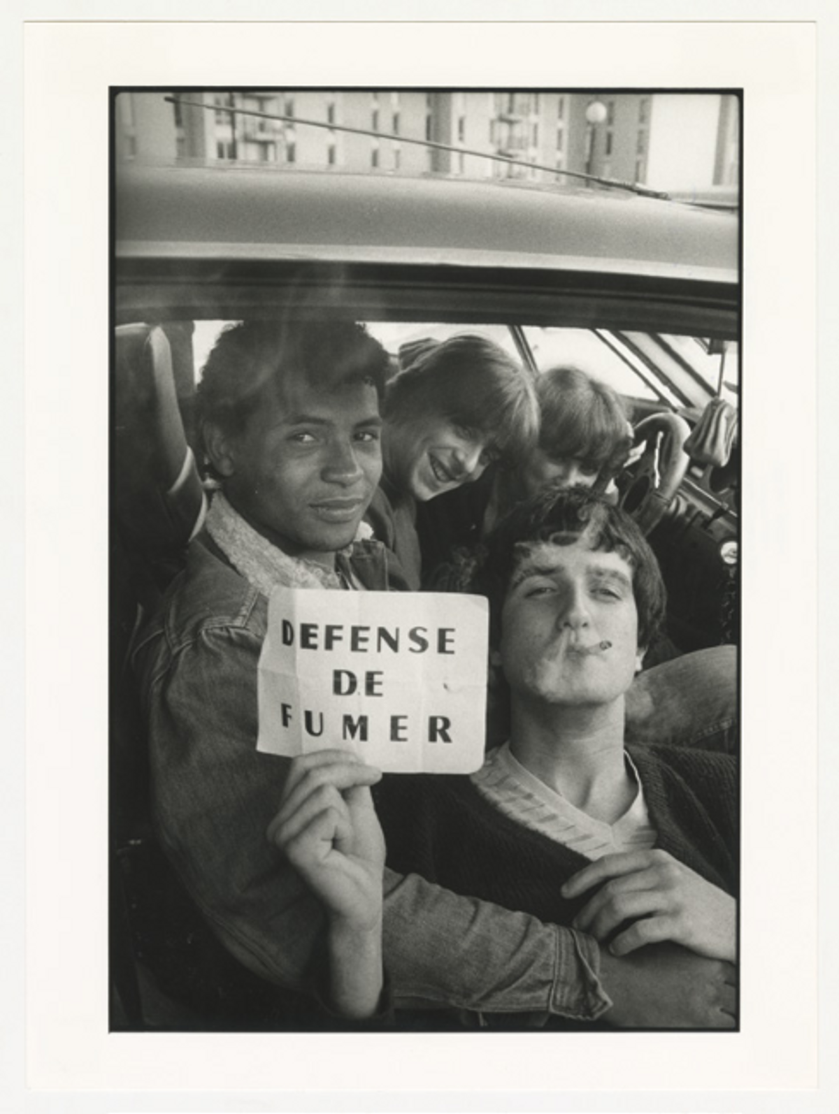 Sabine Weiss, Jeunes Gens fumant dans une voiture et tenant un écriteau « DÉFENSE DE FUMER », Carros, 20 avril 1983, tirage gélatino-argentique. © Les Arts décoratifs