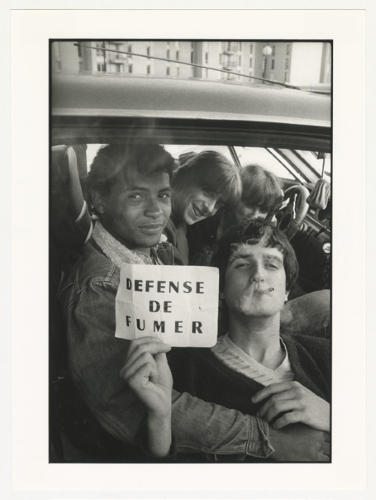 Sabine Weiss, Jeunes Gens fumant dans une voiture et tenant un écriteau « DÉFENSE DE FUMER », Carros, 20 avril 1983, tirage gélatino-argentique. © Les Arts décoratifs