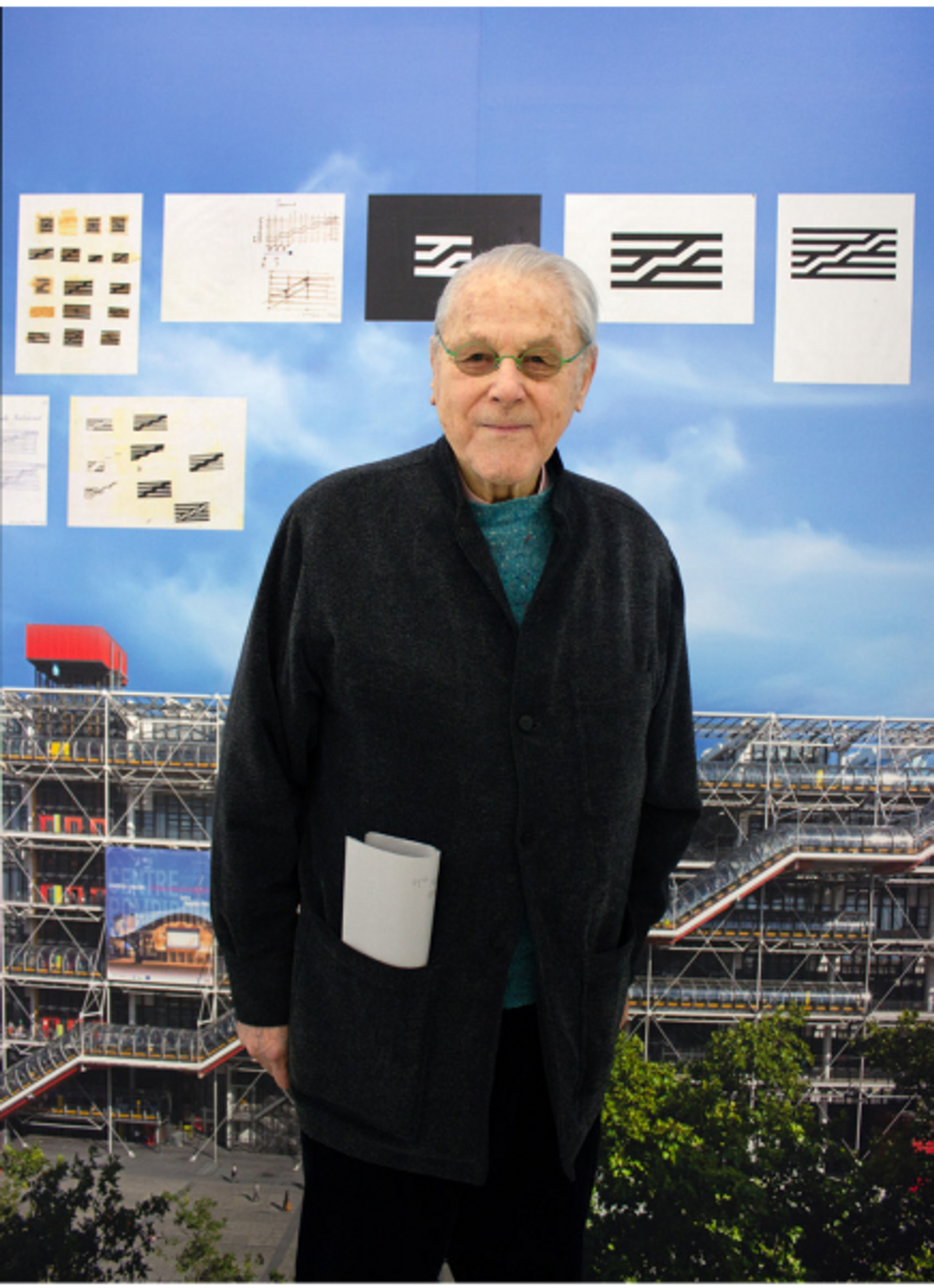 Portrait de Jean Widmer devant les fac-similés de ses études préliminaires du logo du Centre Pompidou. © eac et Centre Pompidou, MNAM-CCI/Dist. RMN-GP/Philippe Migeat