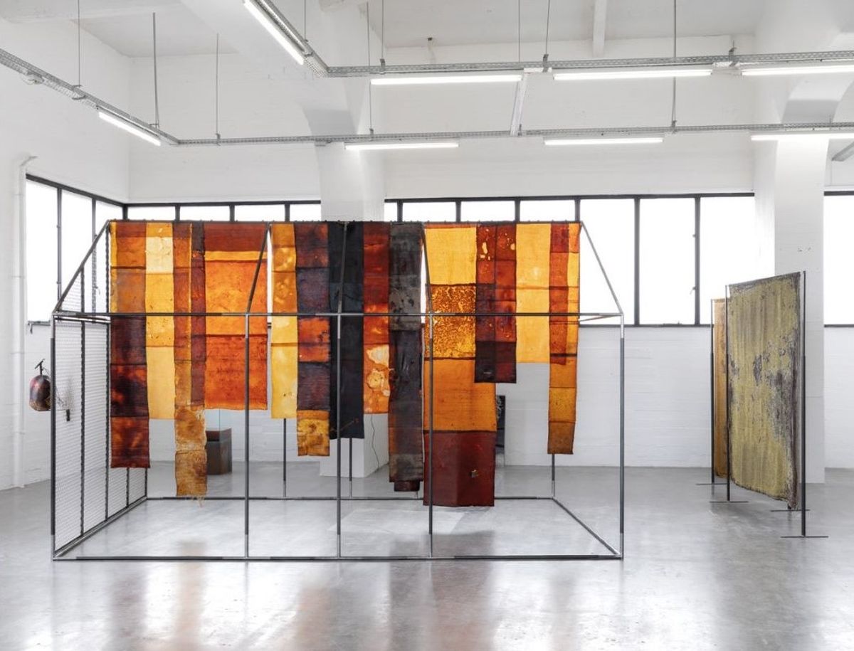 Vue de l’installation OIKOS d’Anne Marie Maes ; au premier plan : Sensorial Skins, 2025, structure métallique, peaux microbiennes et cuirs végétaux ; à droite : Microbial Ancestors (green & orange), 2023, tapisseries Jacquard, WIELS, Bruxelles, 2025. © Anne-Marie Maes. Courtesy du WIELS. Photo Eline Willaert