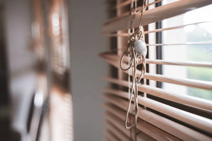 A set of broken blinds with a tangled cord covering a window.