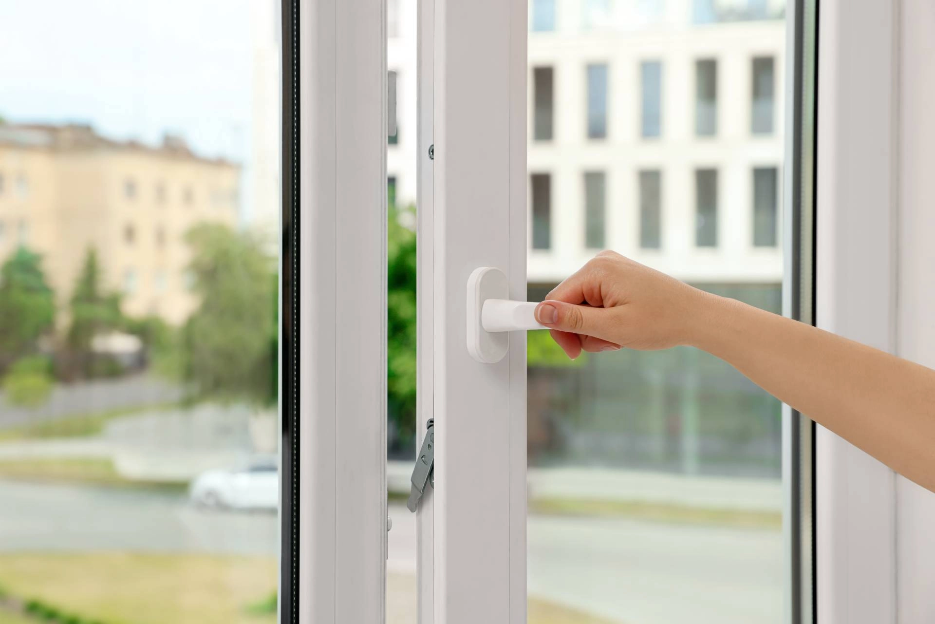 A person's hand opening a casement window that's in need of a window shade