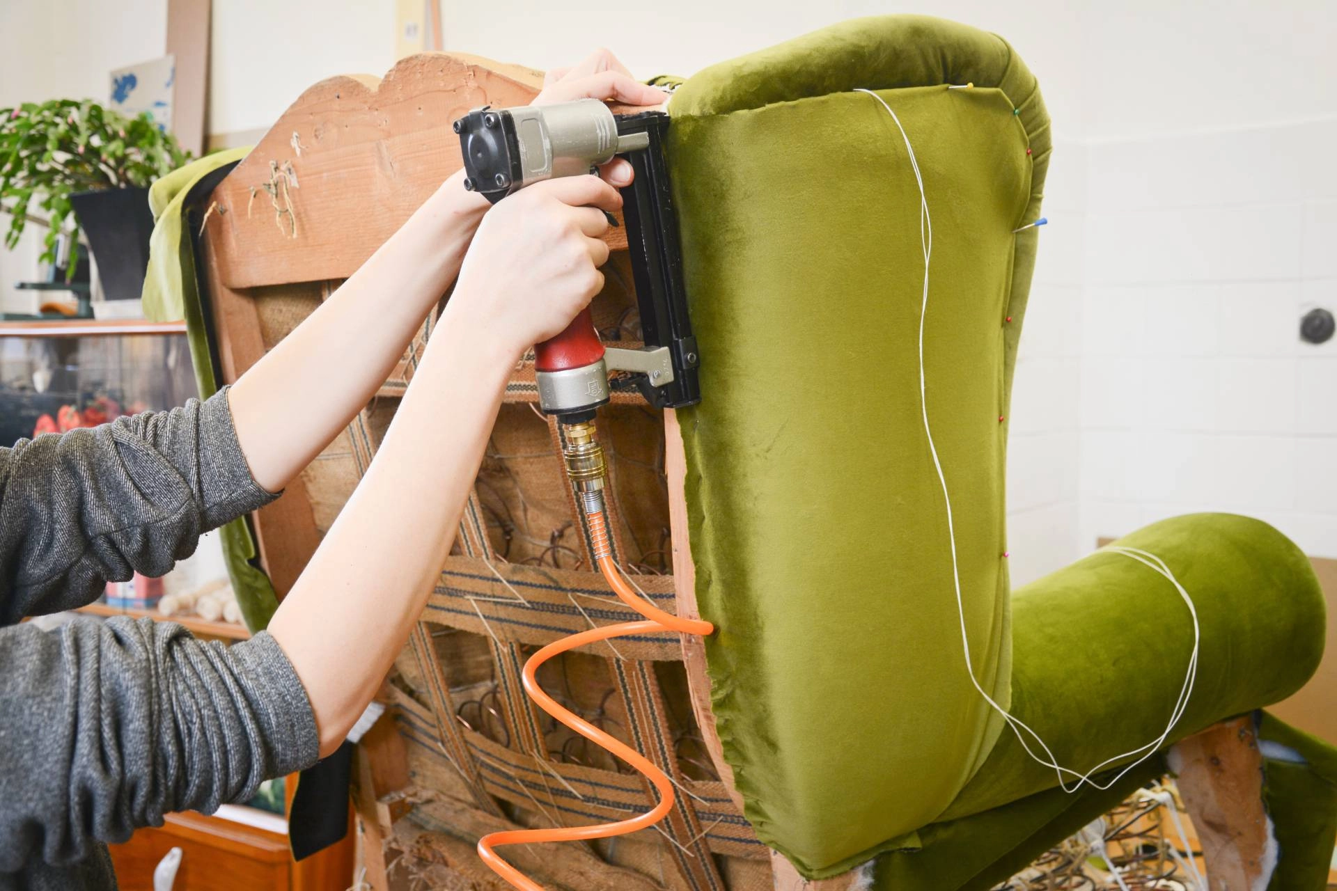 A professional performing custom upholstery services, attaching green fabric to a winged sitting chair