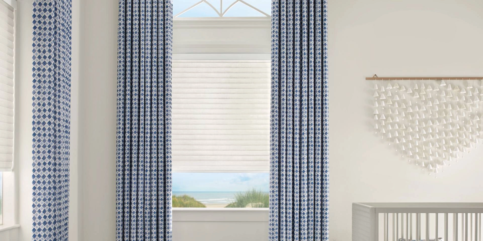 Child-safe window treatments with automated shades paired with patterned drapes in a bright and airy nursery