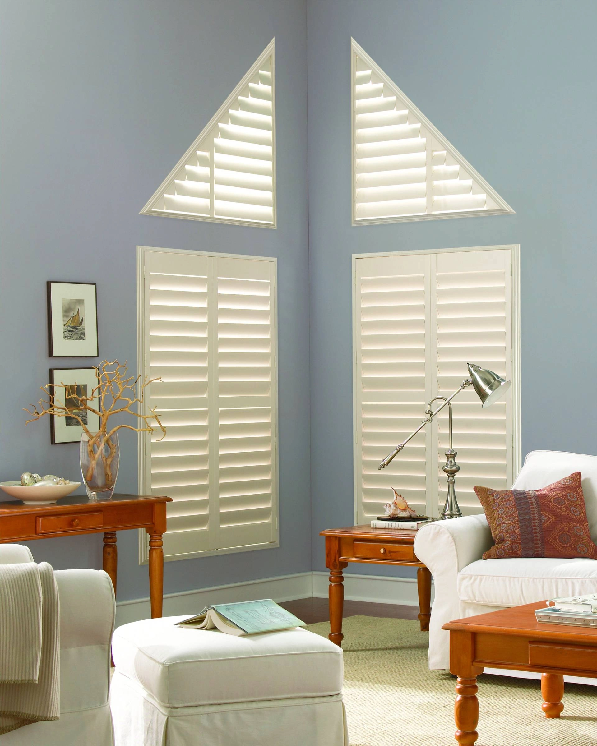 Palm Beach™ Polysatin™ shutters on angled triangle windows and rectangular windows in a coastal living room.