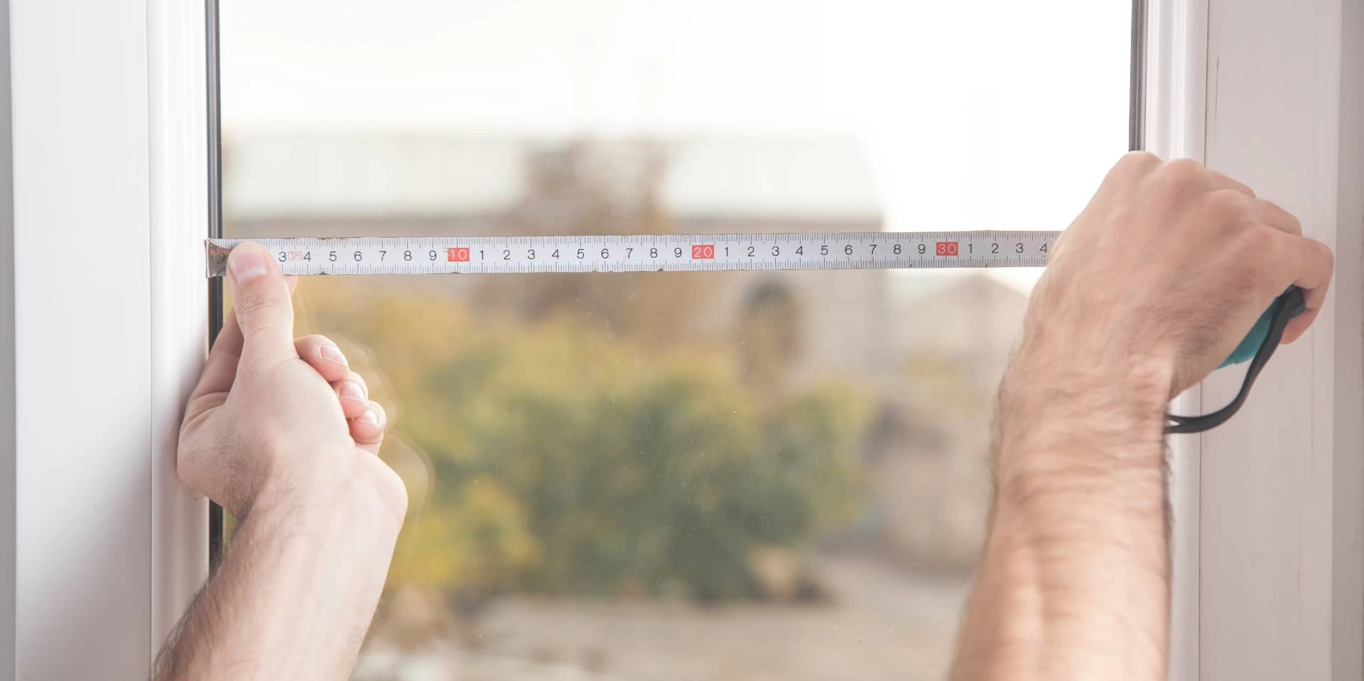 Person's hands using a measuring tape to take accurate measurements of a window for new blinds