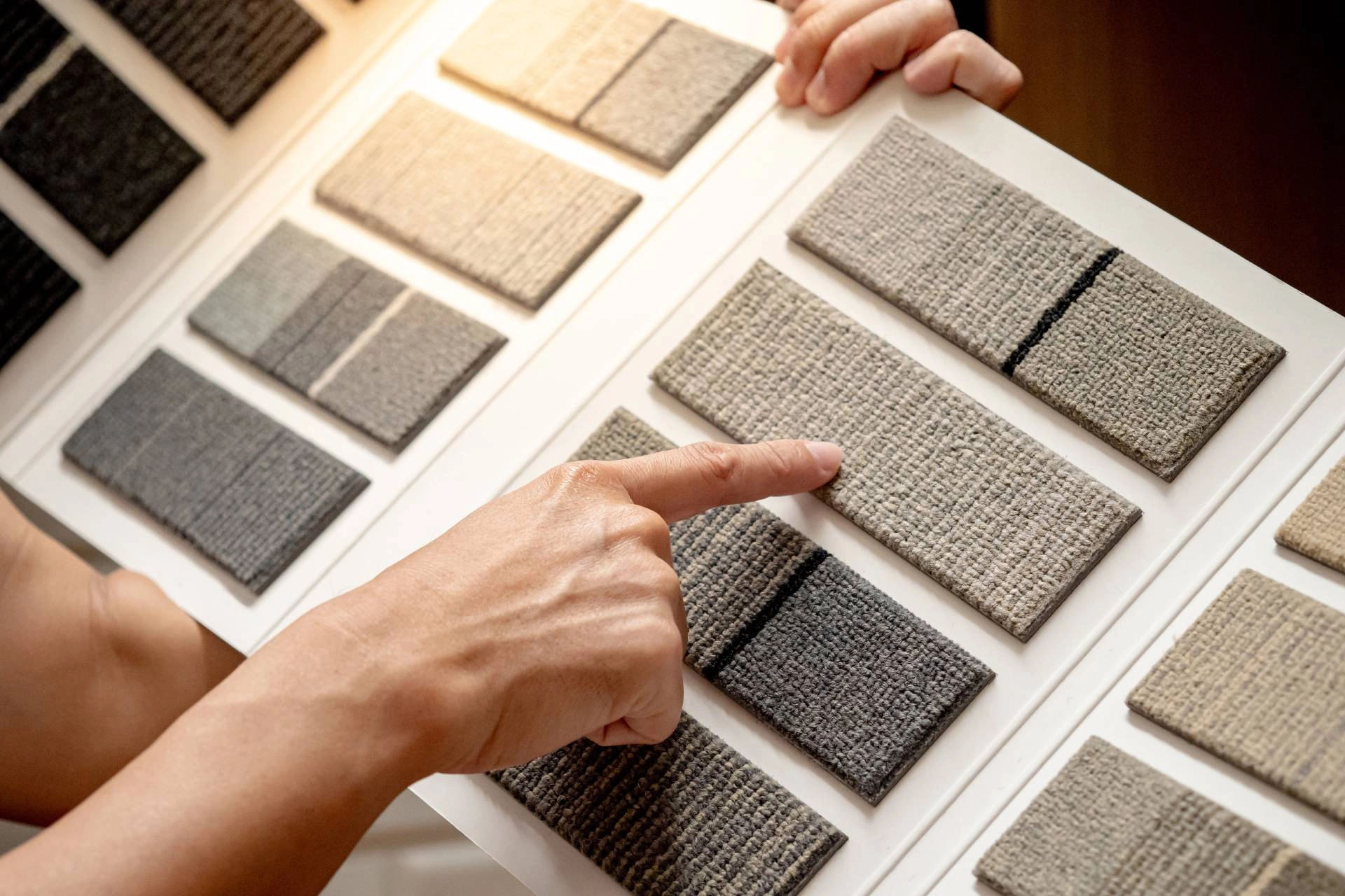 Person holding a sample book containing various types of carpeting swatches and pointing to one