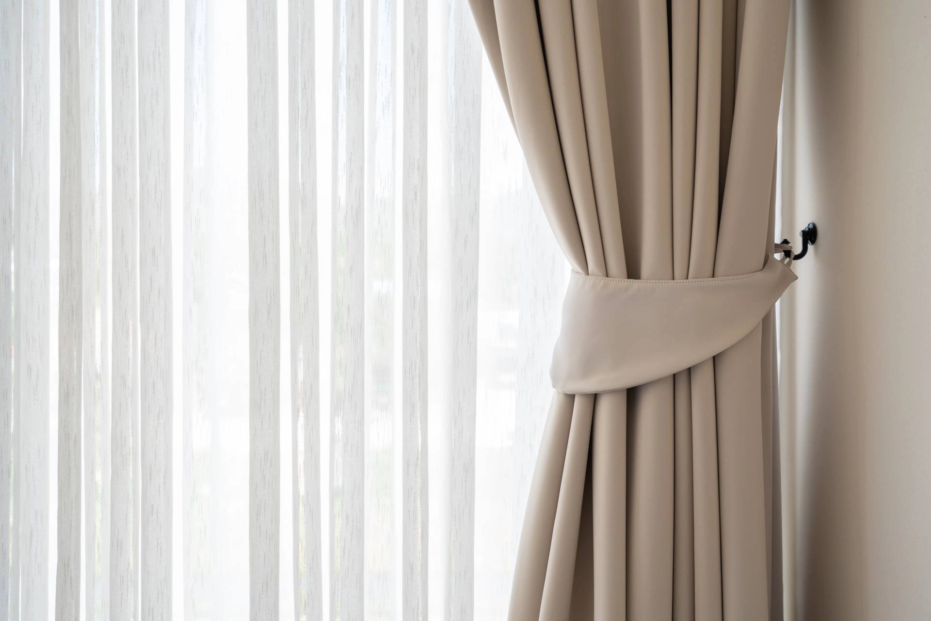 Solid custom drapery layered with a sheer drape with visible drapery hardware, holding the drape back