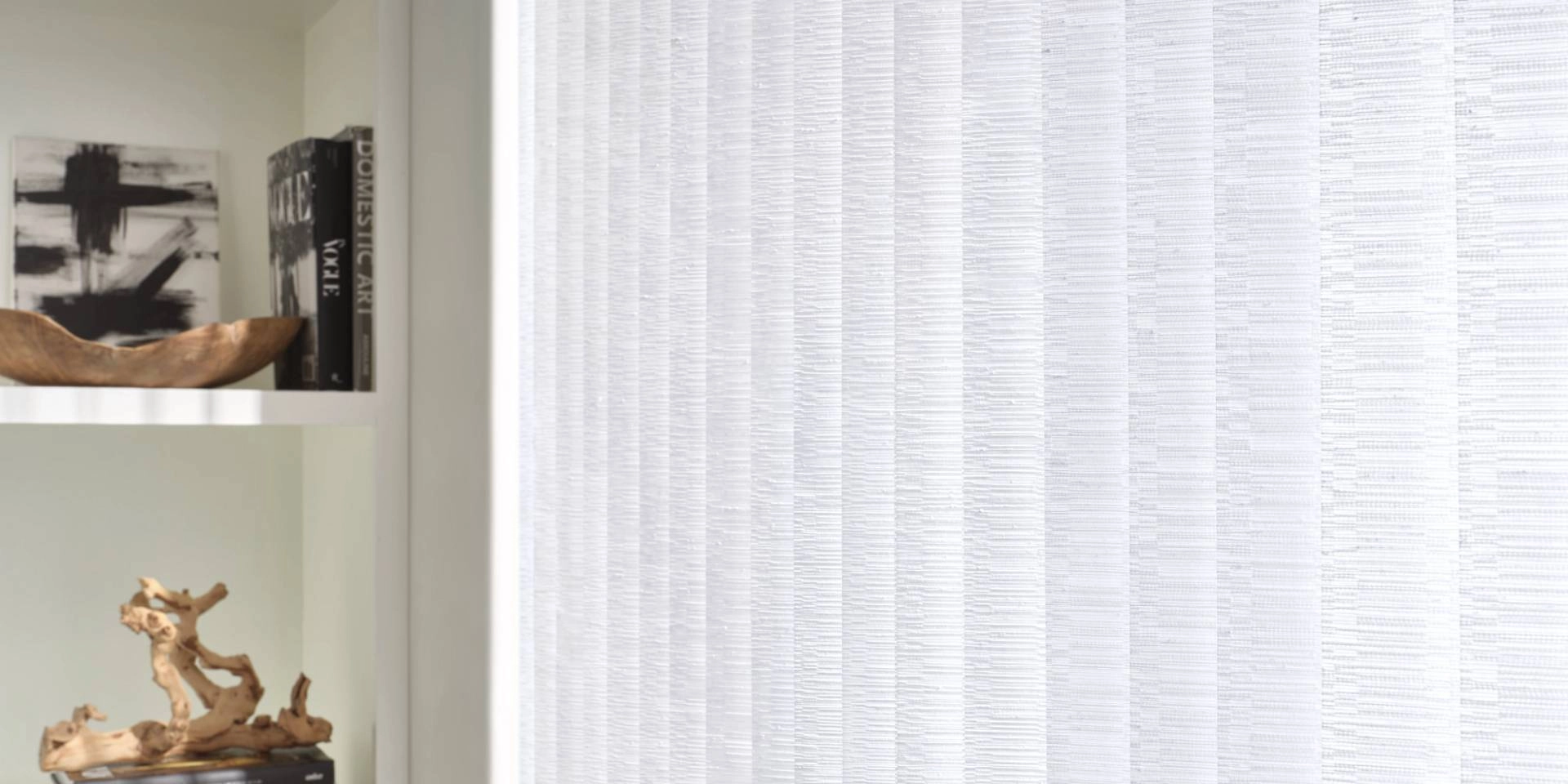 An up-close image of custom Hunter Douglas Somner® Vertical Blinds beside a styled bookshelf