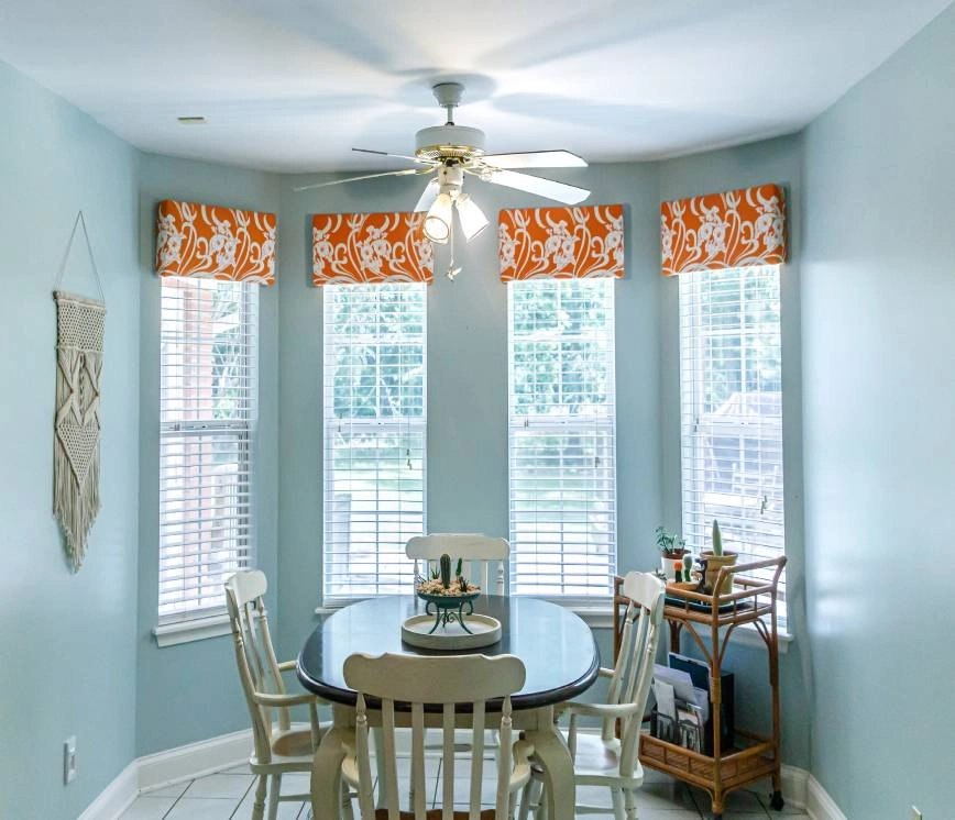 Eat-in kitchen with light blue walls and four windows, adorned with blinds and orange valances near Springfield, IL