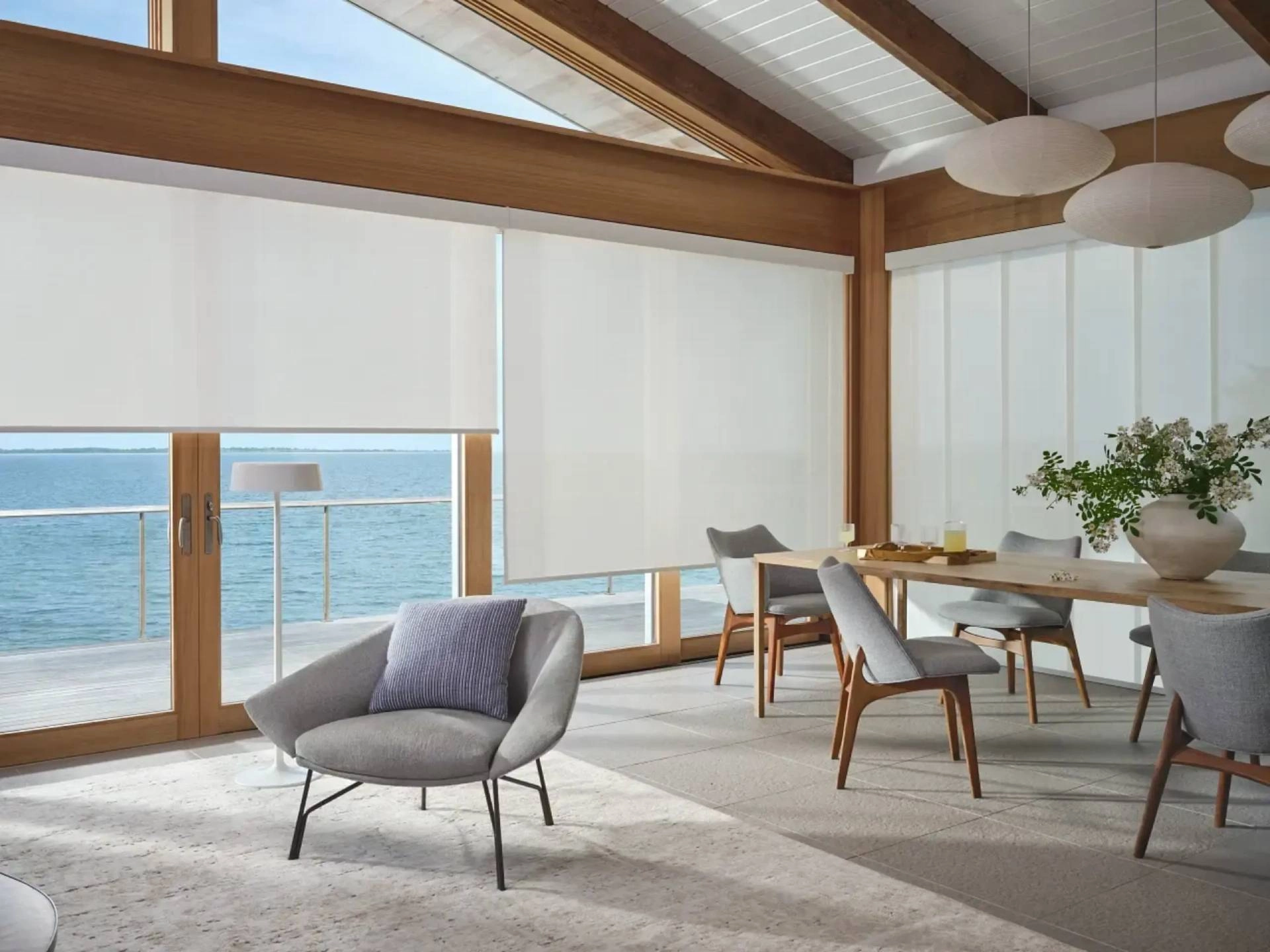 Designer Solar Shades on floor-to-ceiling windows in a bright coastal dining room.