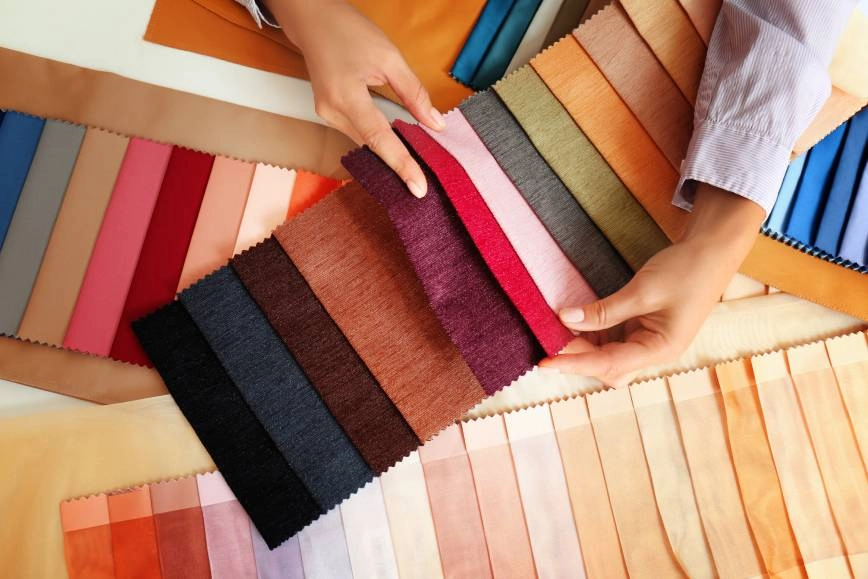 Collection of various colored and textured custom fabric swatches on a table with a person's arms