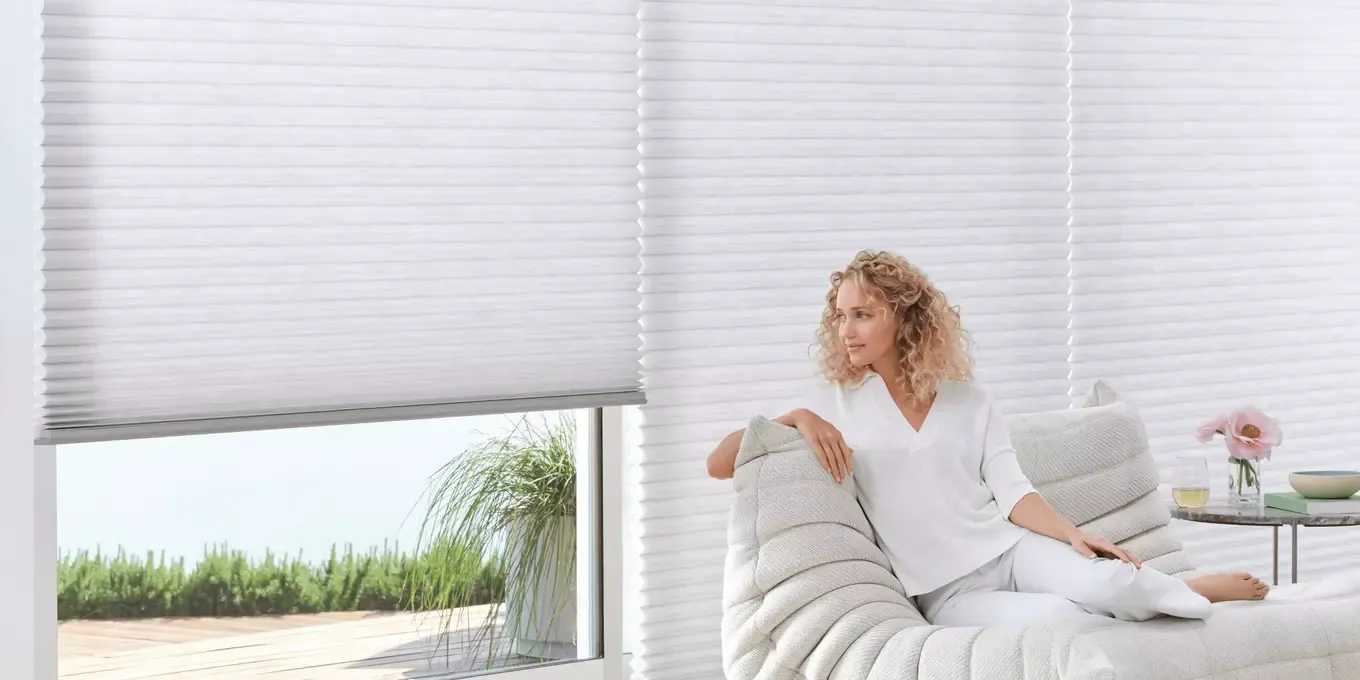 A women sitting on a couch looking out windows featuring Hunter Douglas shades.