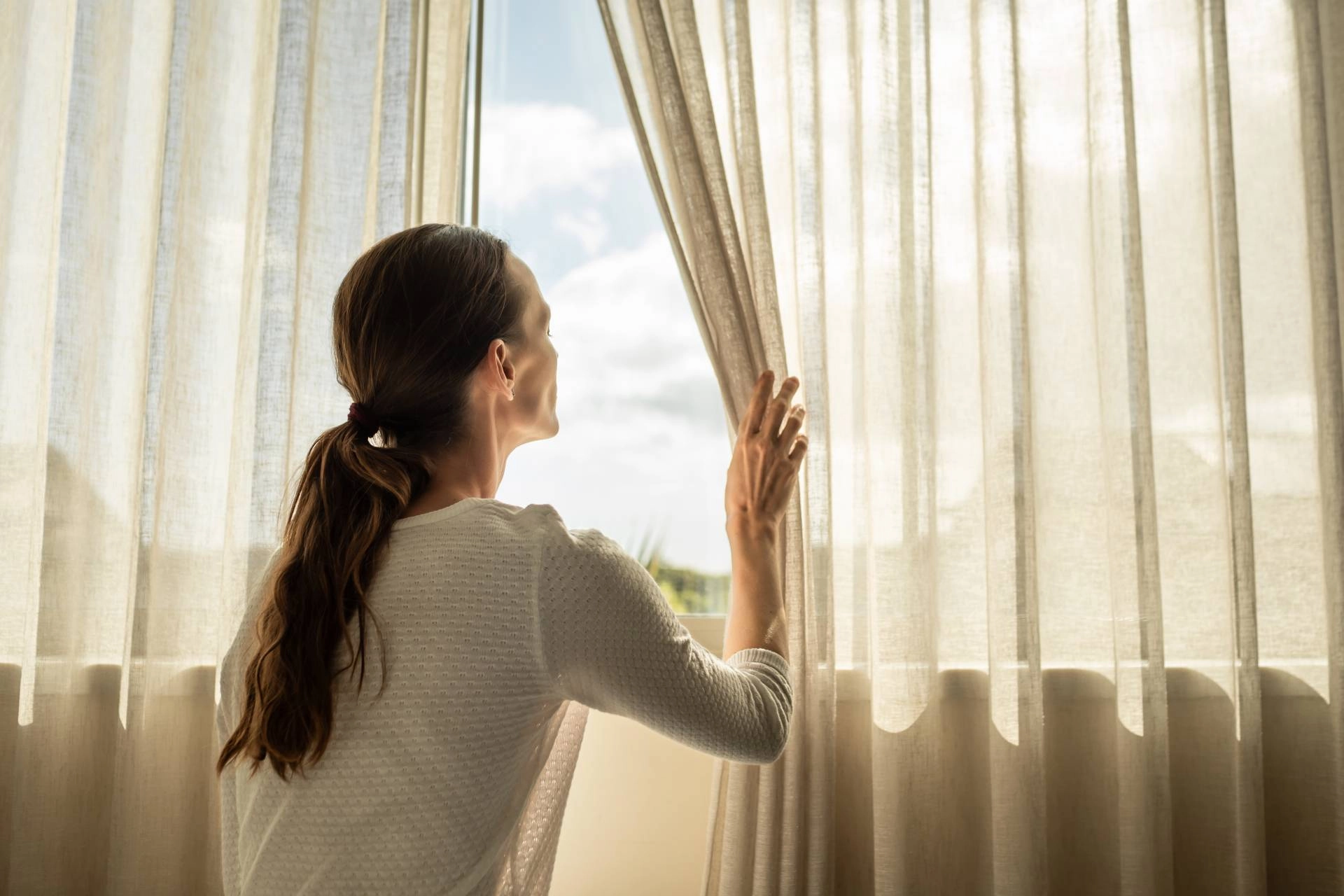 Someone standing at a window, moving the pleated curtains near O’Fallon, MO