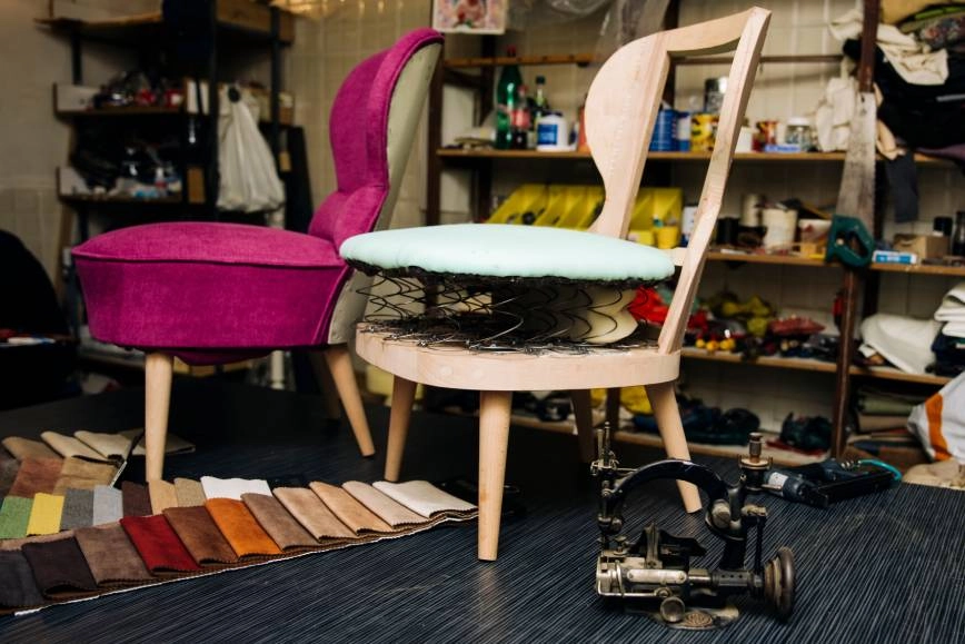 Image of two accent chairs, one pink and one in progress, in an upholstery workshop