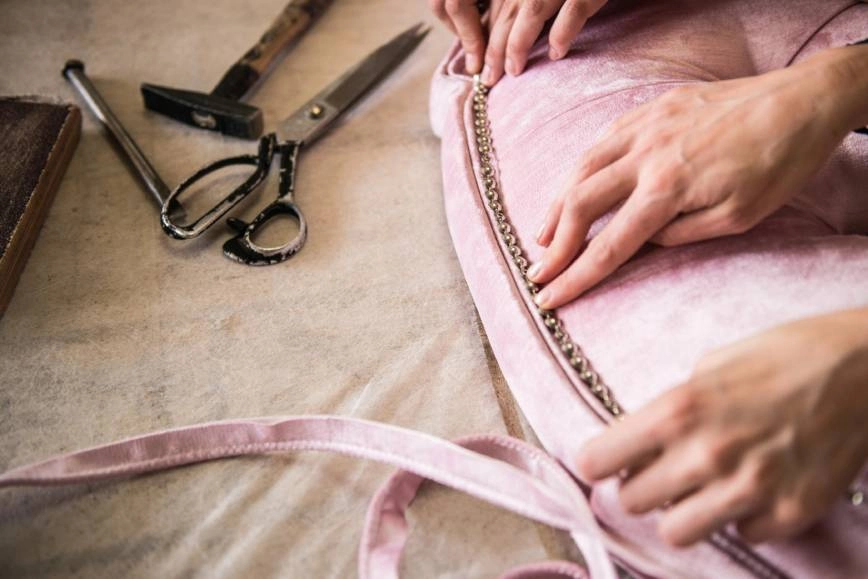 A detailed image of an upholstery expert adding beaded trim to light pink fabric