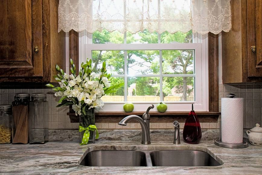 An image of a sheer, white lace valance for a window above a home's kitchen sink