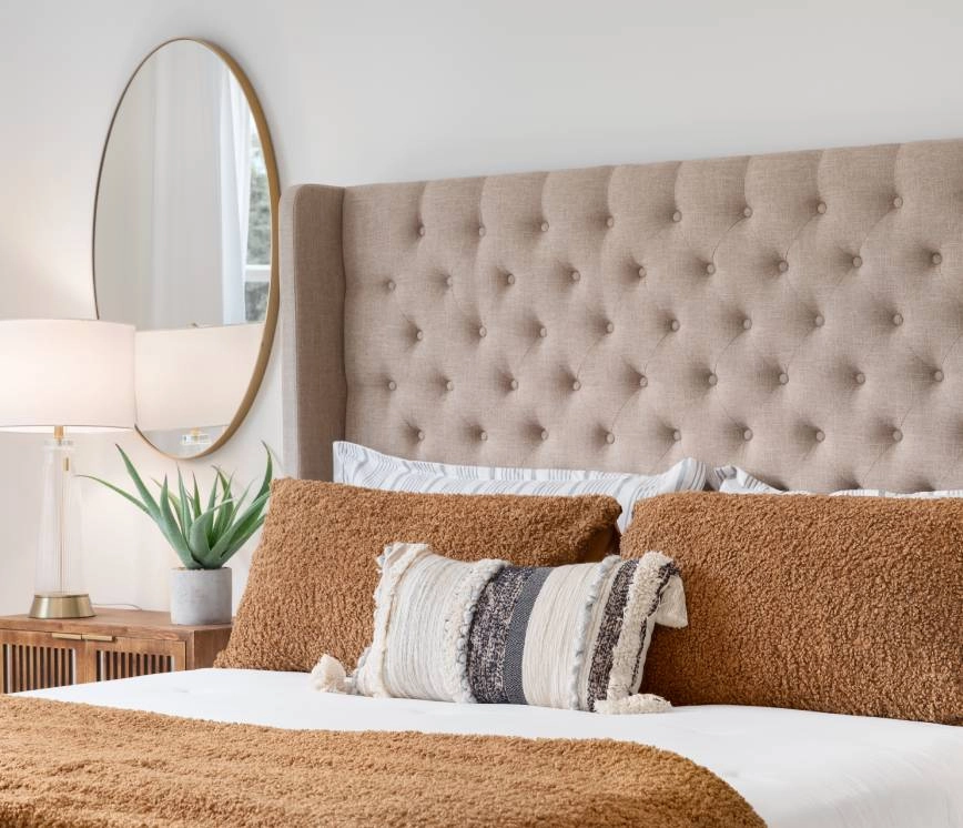 Staged bedroom with brown throw pillows and quilt, tufted headboard, and wall mirror near Fort Myers, FL