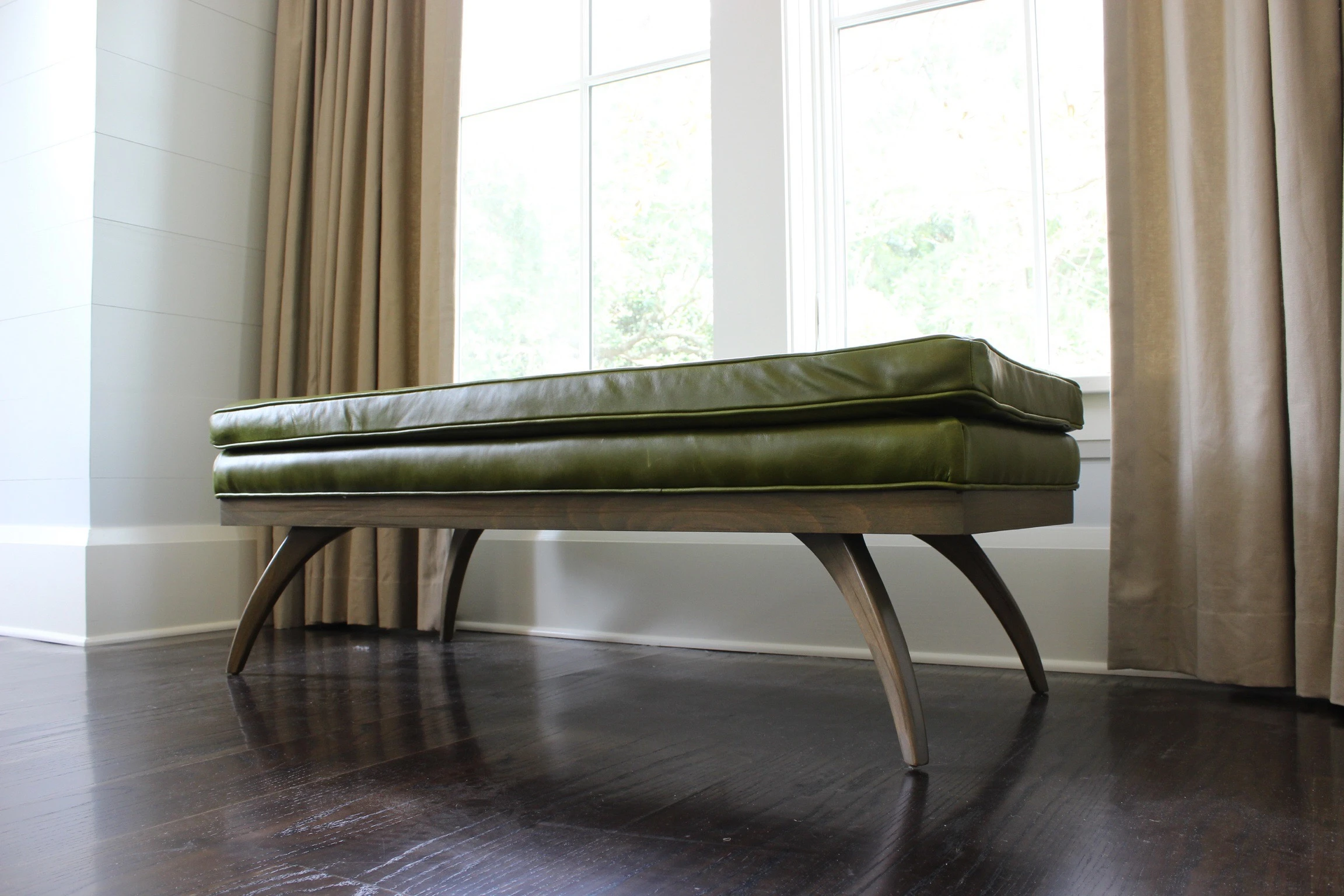 A bench in front of windows with drapery.