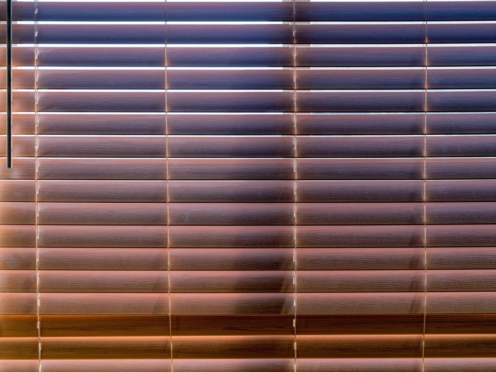 A set of faux wood Venetian-style blinds with sunlight streaming through near Quincy, IL