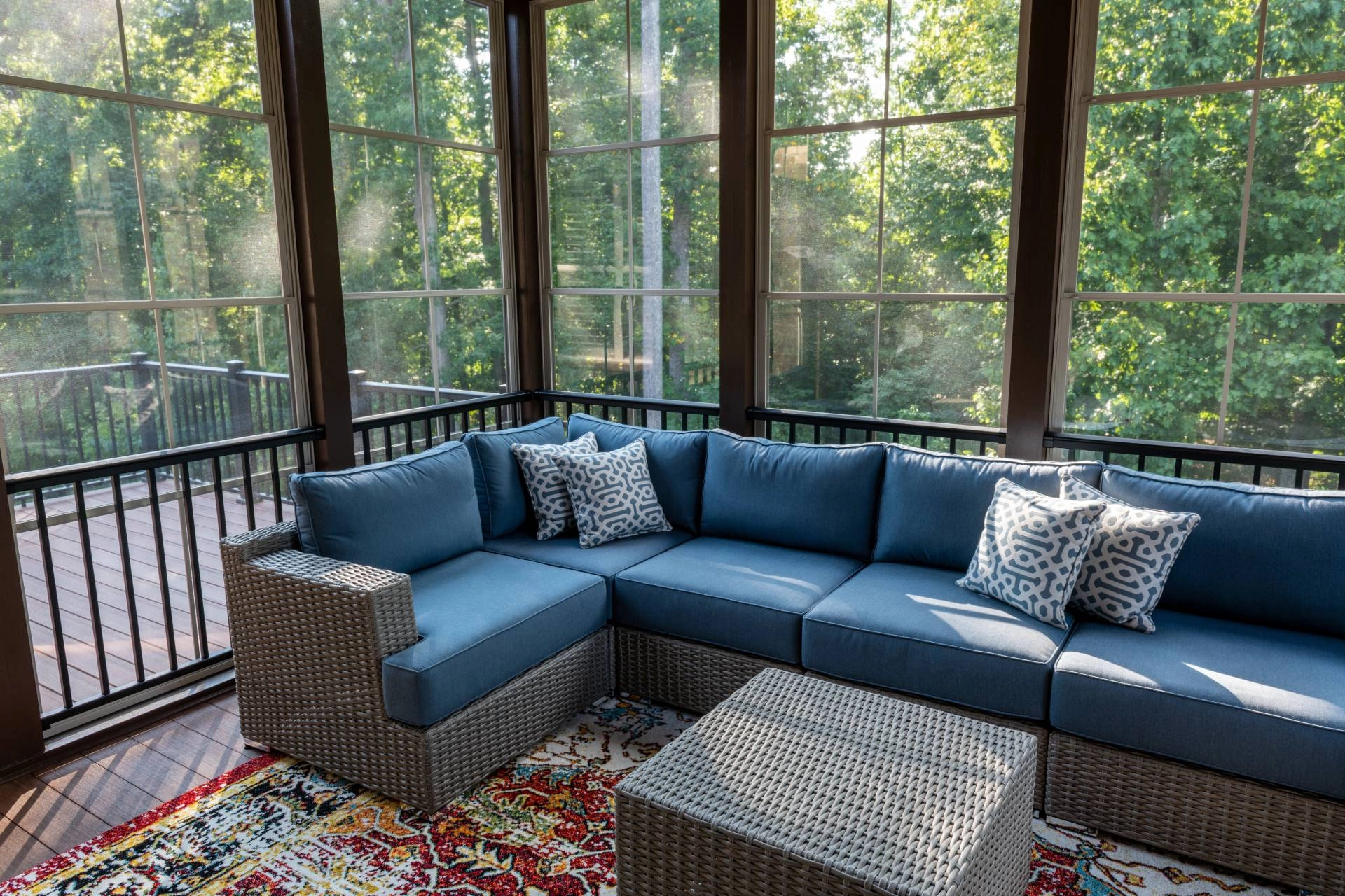 A sunroom, surrounded by lush green trees, with expansive windows in need of proper window treatments