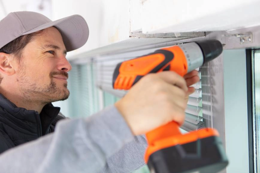 Window treatment worker repairing window blinds with a drill .
