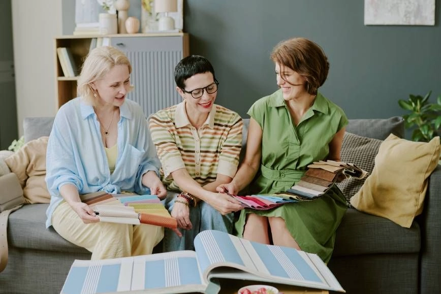 Three women sitting on a couch exploring custom fabrics for their home decor with a designer