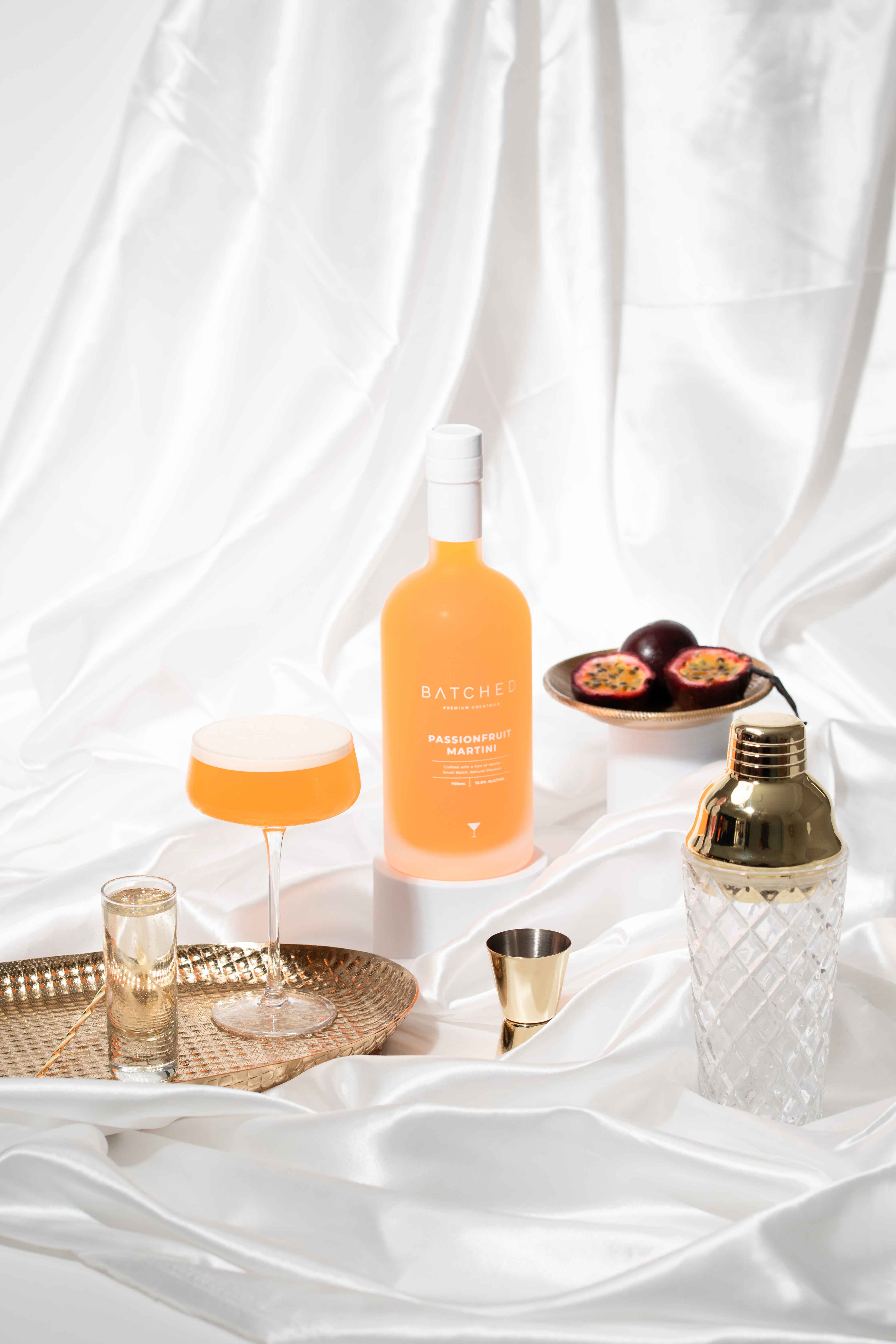 Batched Passionfruit Martini on picnic cloth with shaker, passionfruit and wine bottle