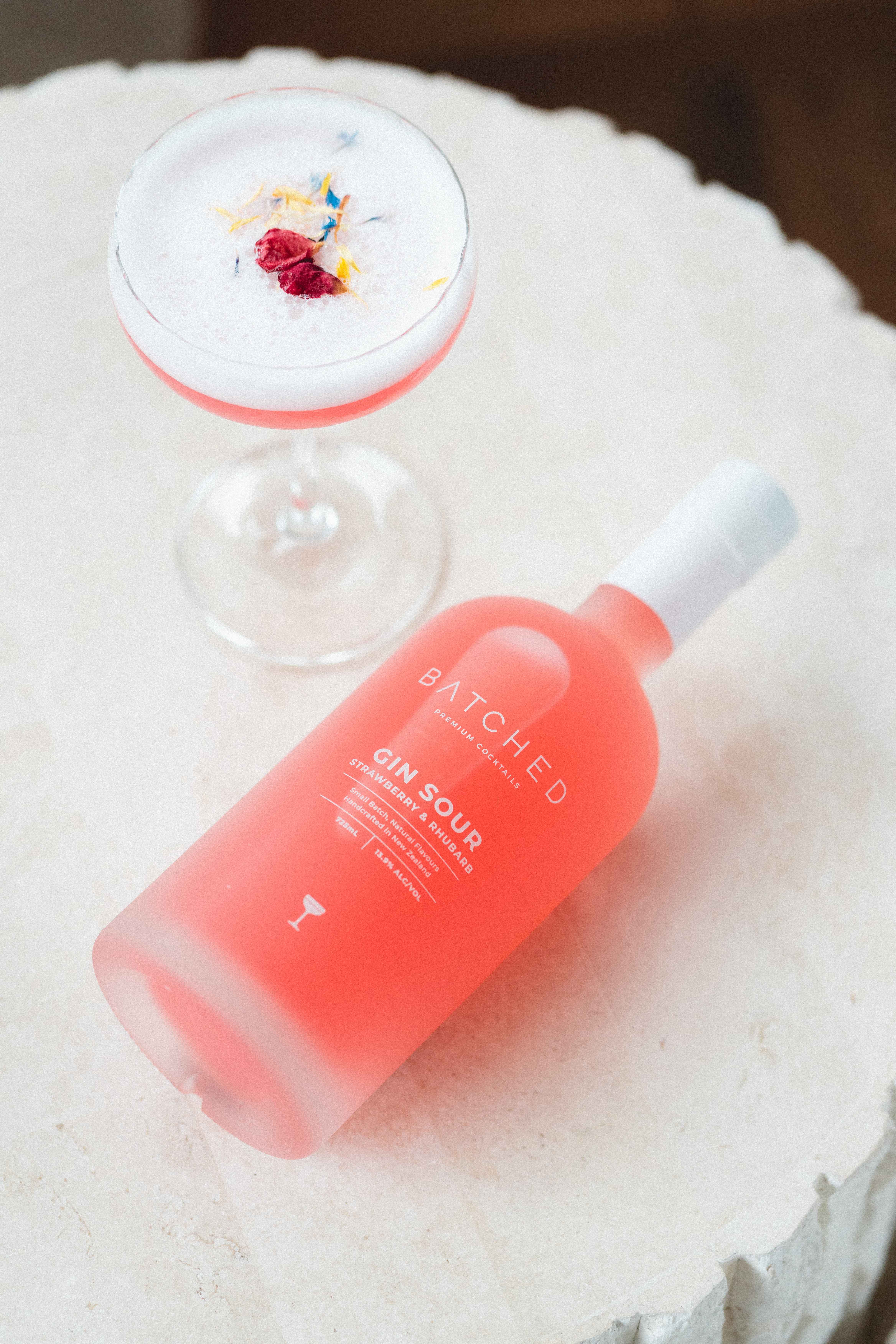 Batched Gin Sour bottle lying on table with drink served in martini glass