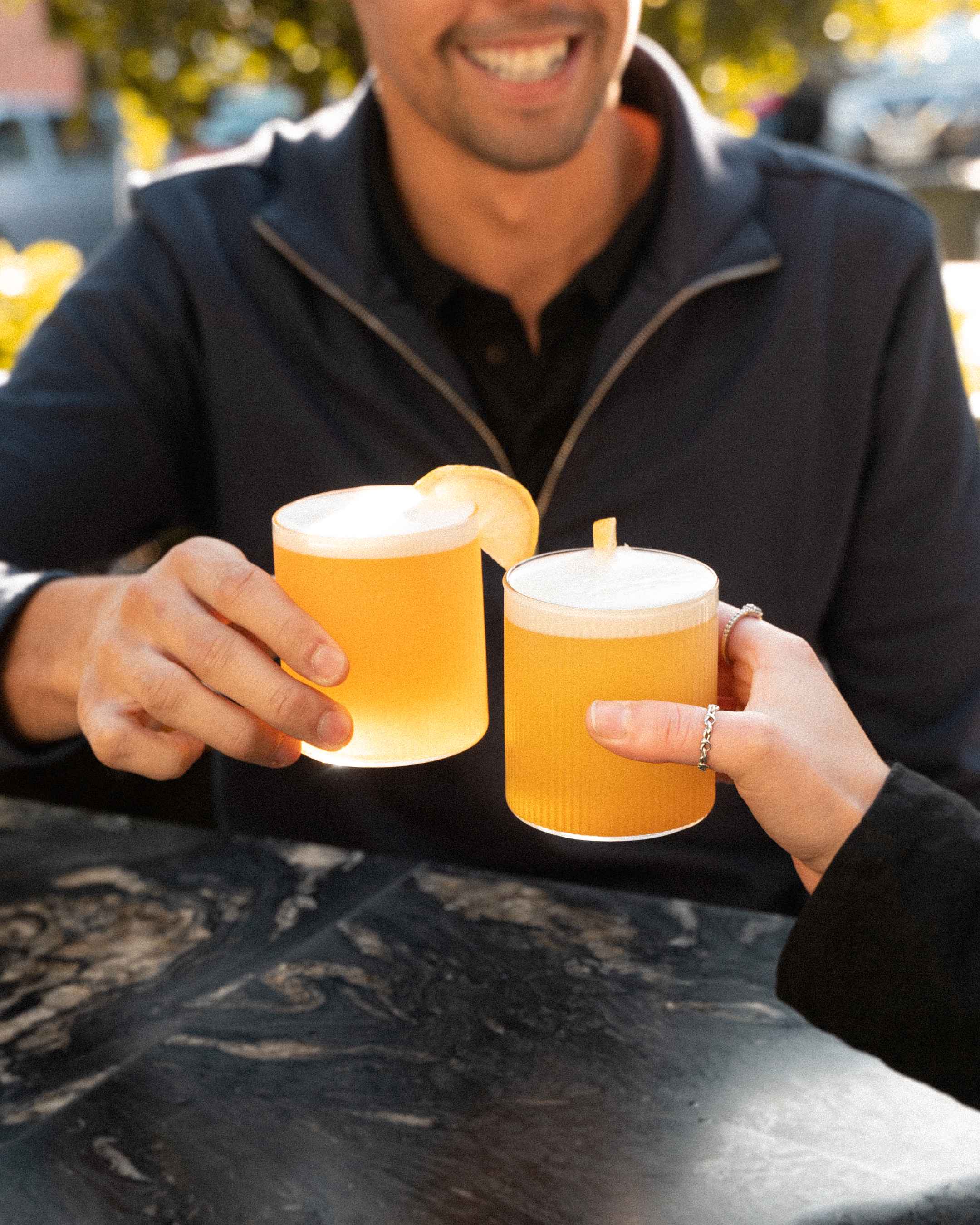 Batched Whiskey Sour in glasses being held by two people