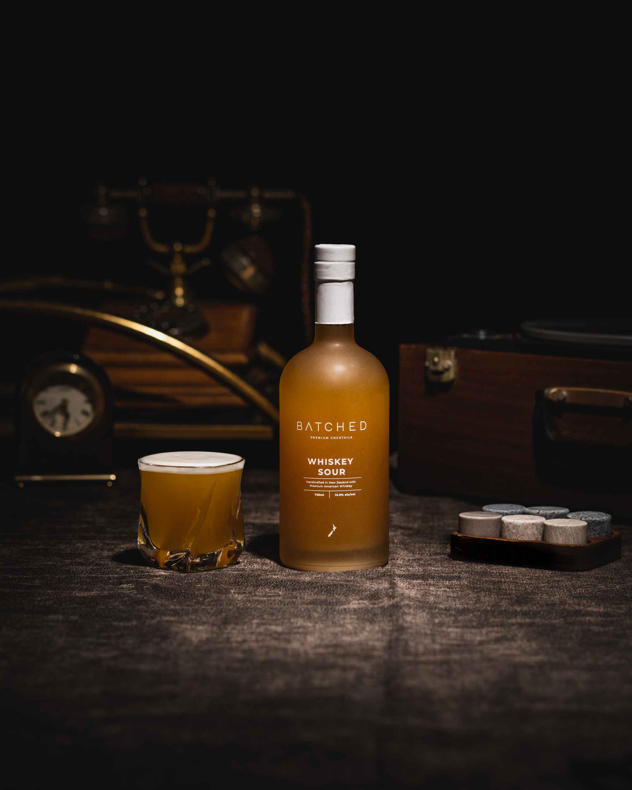 Batched Whiskey Sour bottle with drink served in glass on bench