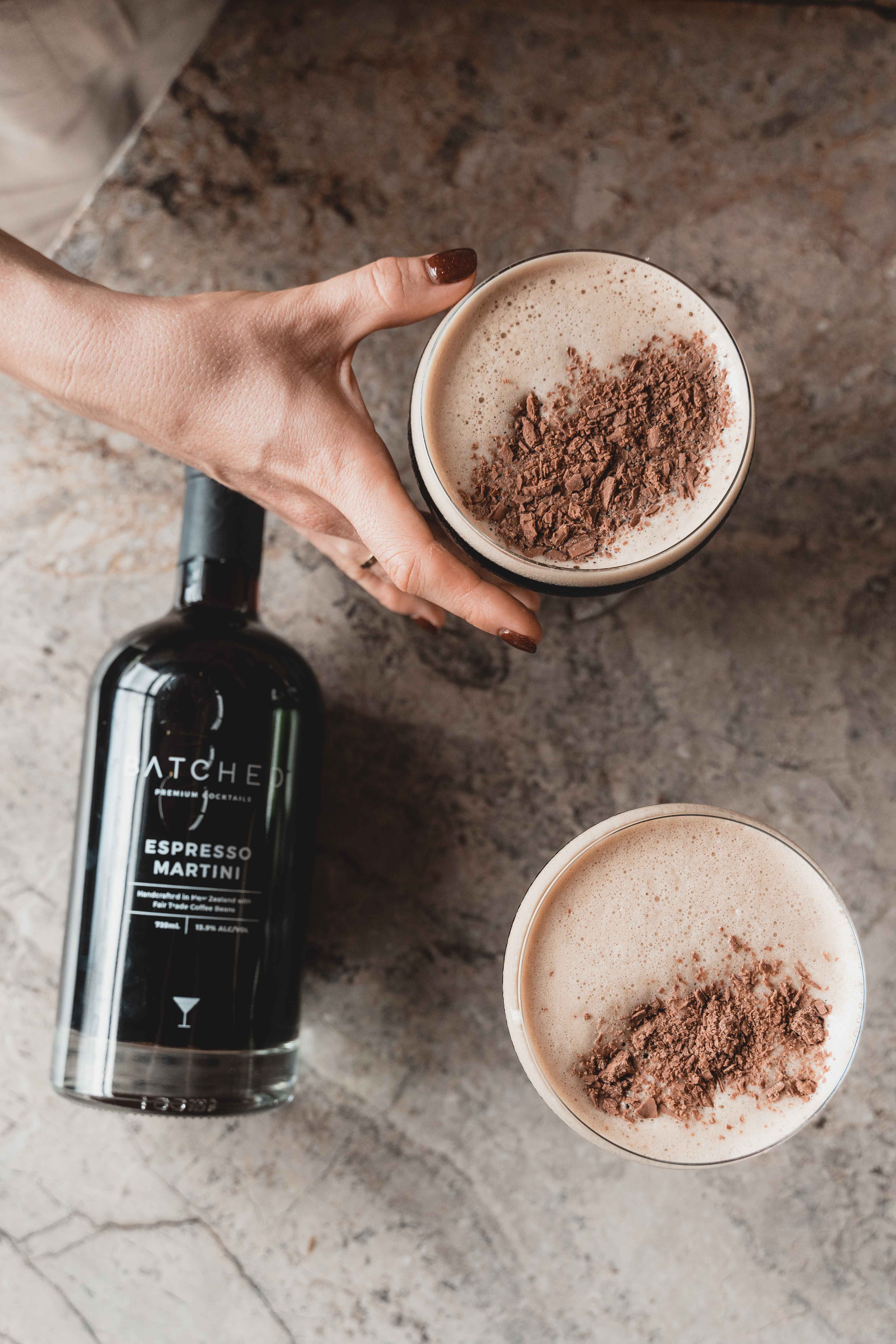 Hand grabbing Batched Espresso Martini served in glass with garnish