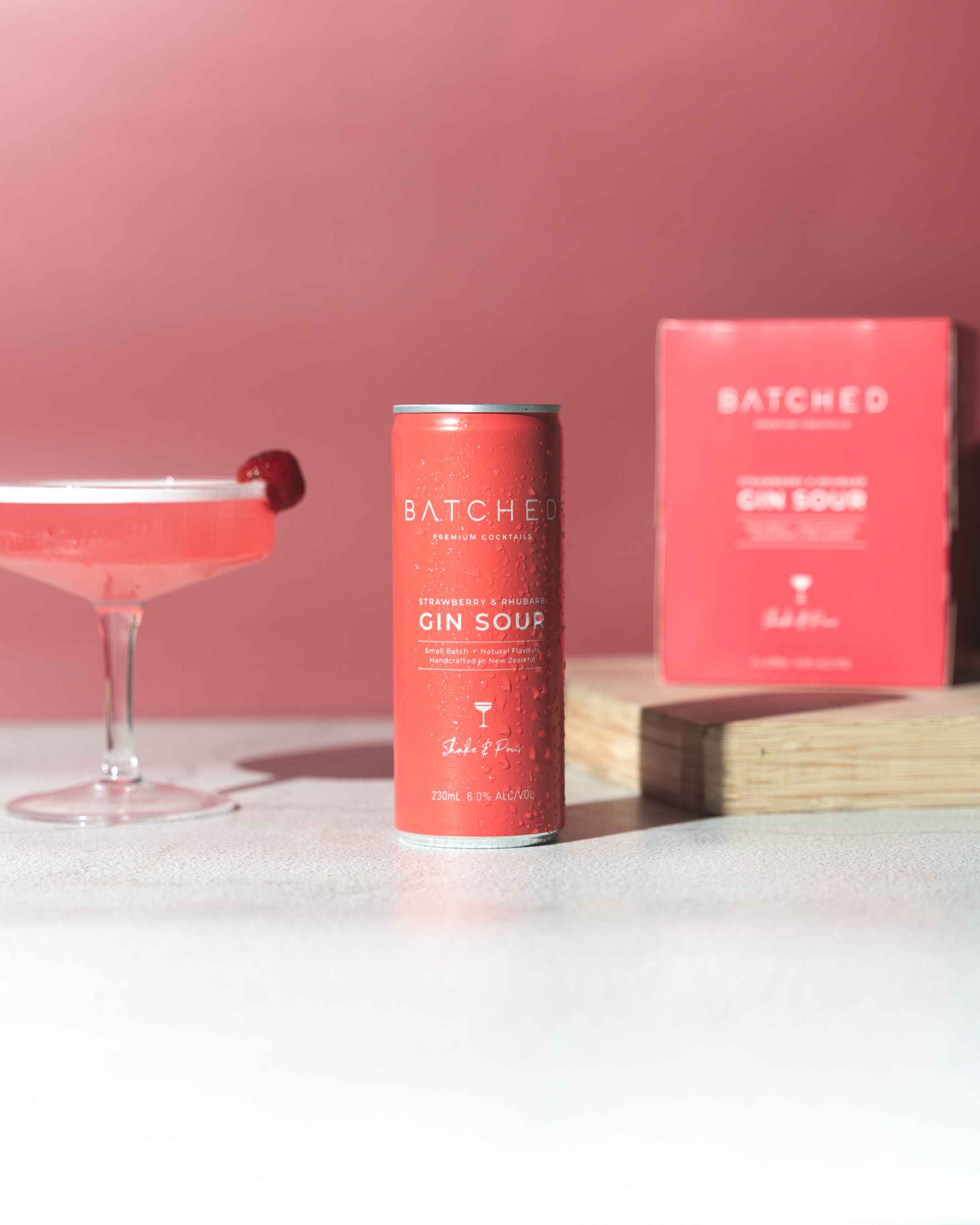 Batched Gin Sour can on table with box and martini glass in pink background 