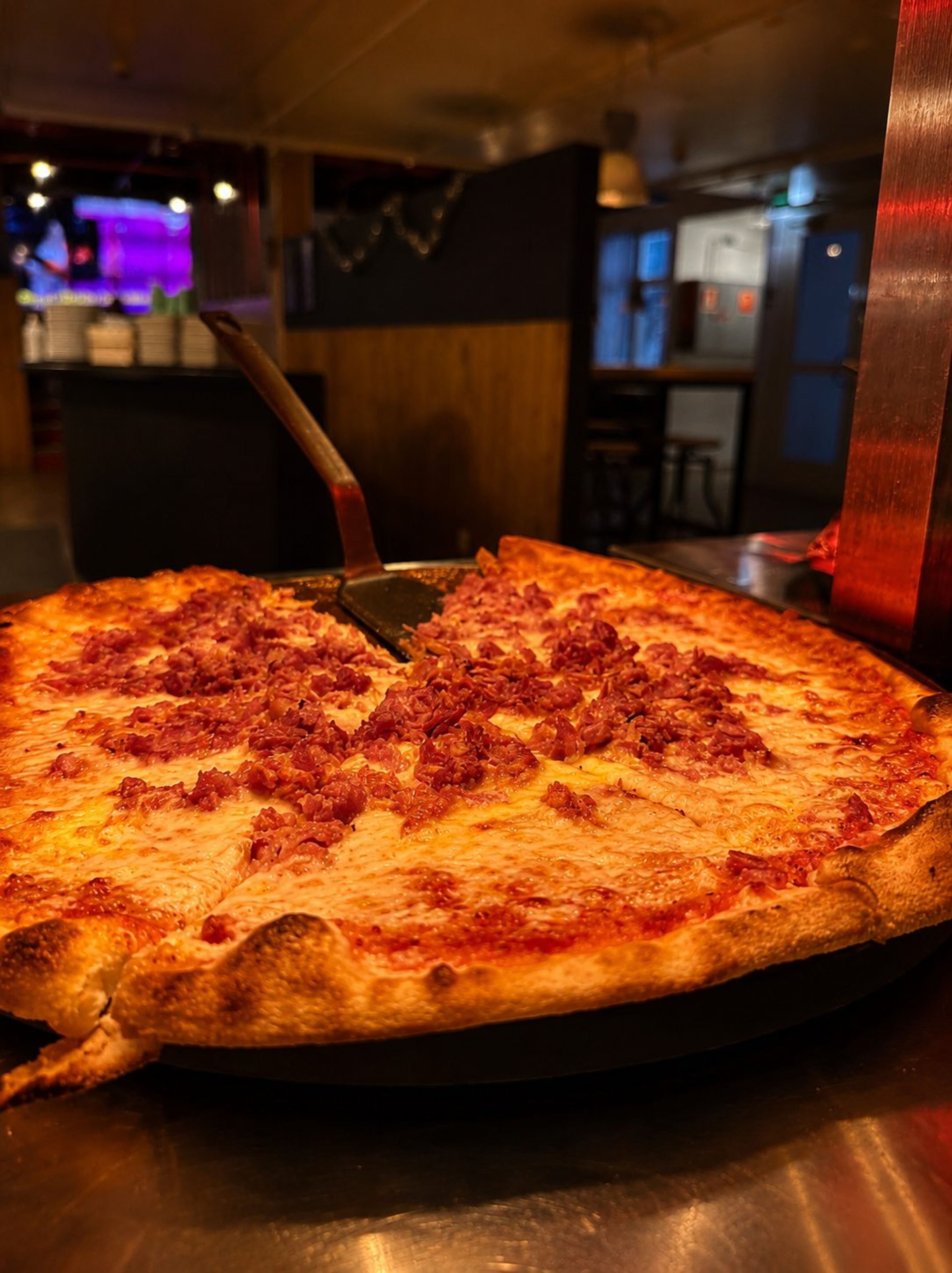 Kokonainen makkarapizza pannulla, taustalla ravintolan sali