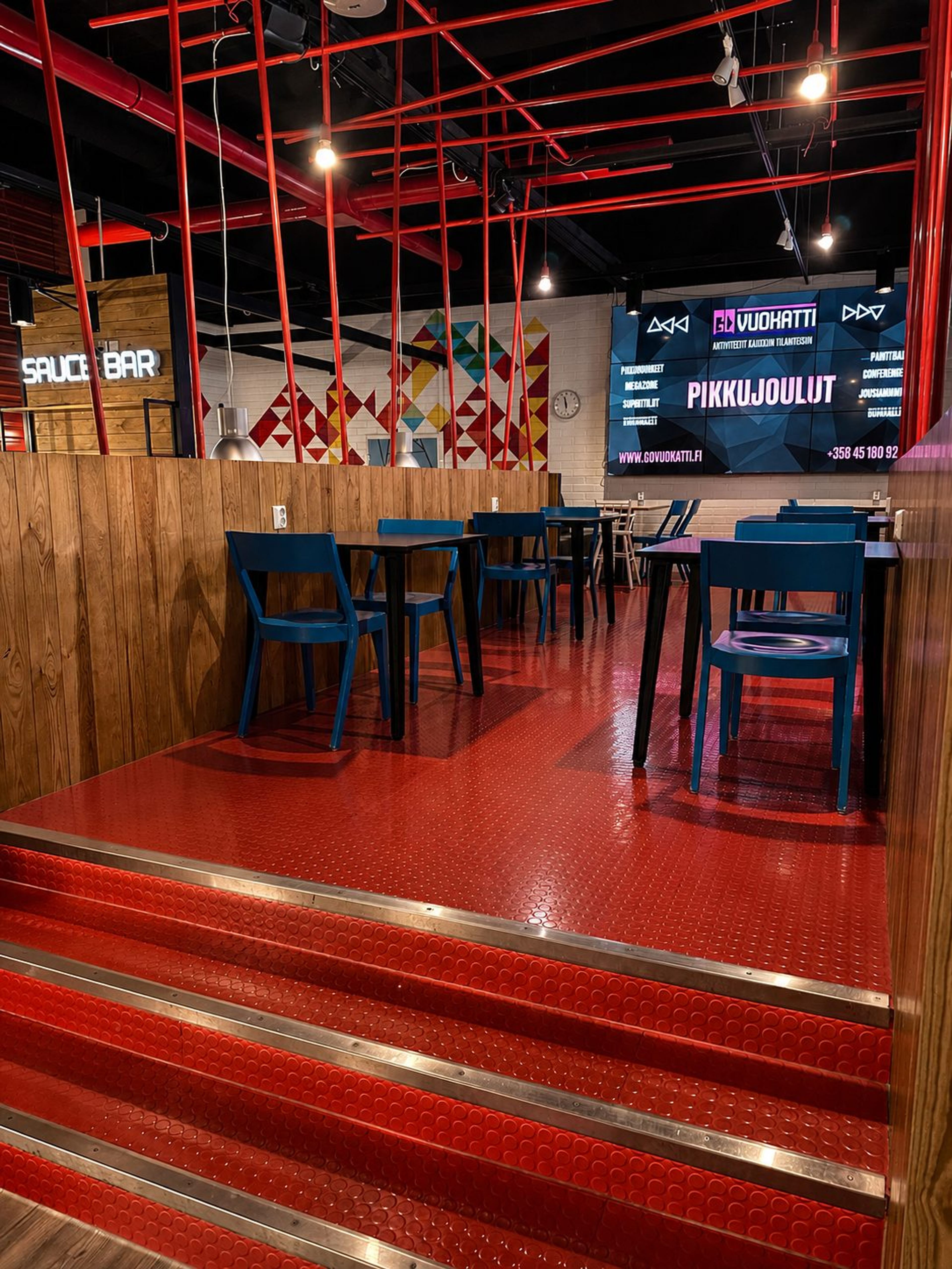 The raised seating area with red flooring and blue chairs, the Sauce Bar sign behind