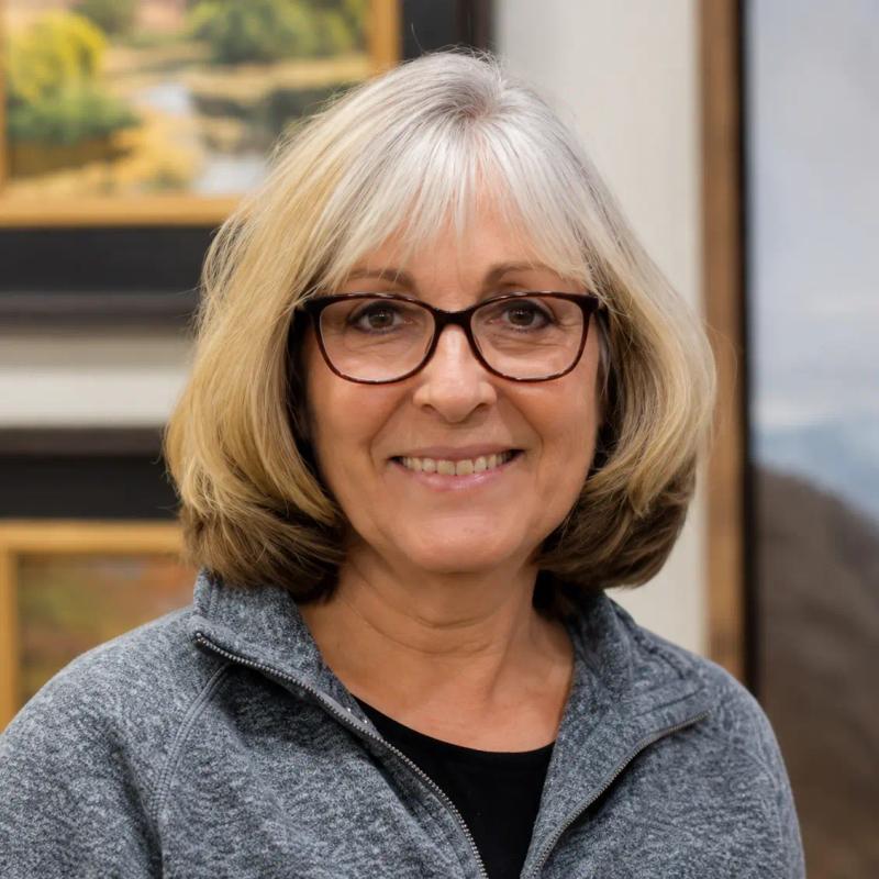 smiling woman with glasses posing in front of framed coastal paintings in an art gallery