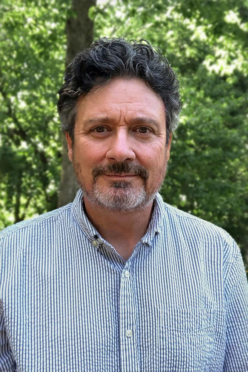 smiling man outdoors in striped shirt and green backdrop