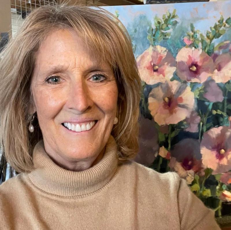 smiling woman posing beside floral painting in art studio