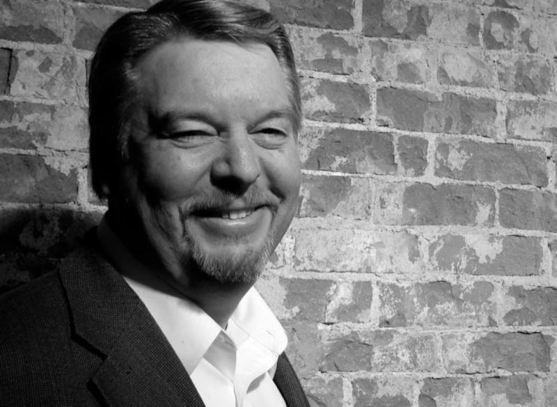 smiling man in black and white portrait by brick wall