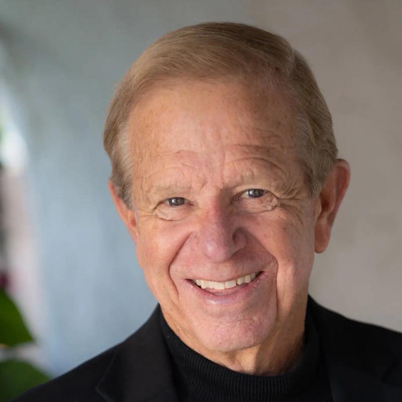 black and white portrait of smiling older man in black blazer and turtleneck sweater