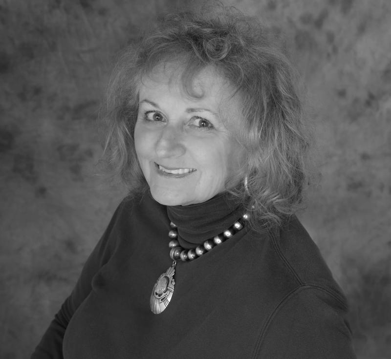 black and white portrait of a woman with curly hair smiling, wearing a turtleneck and a beaded pendant necklace