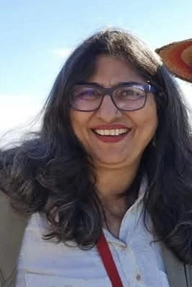 woman with dark hair and glasses smiling outdoors against a bright sky