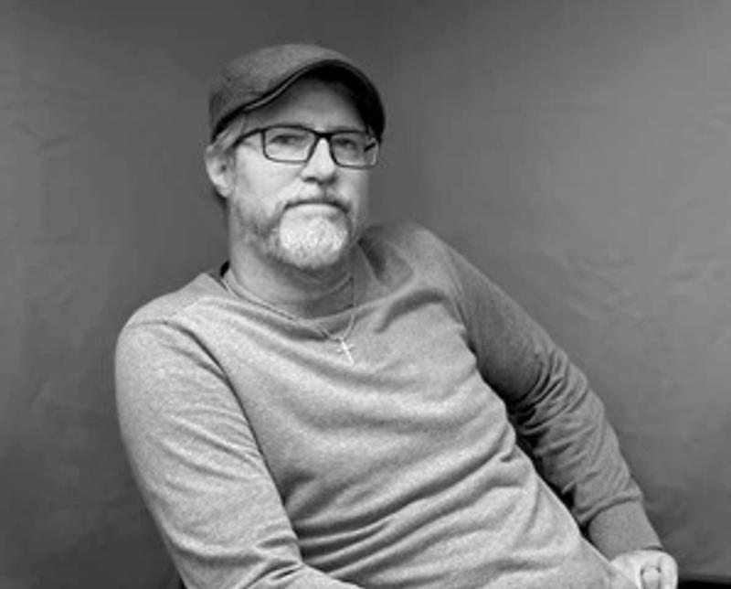 black and white portrait of a man with glasses and beard wearing a cap and long sleeve shirt