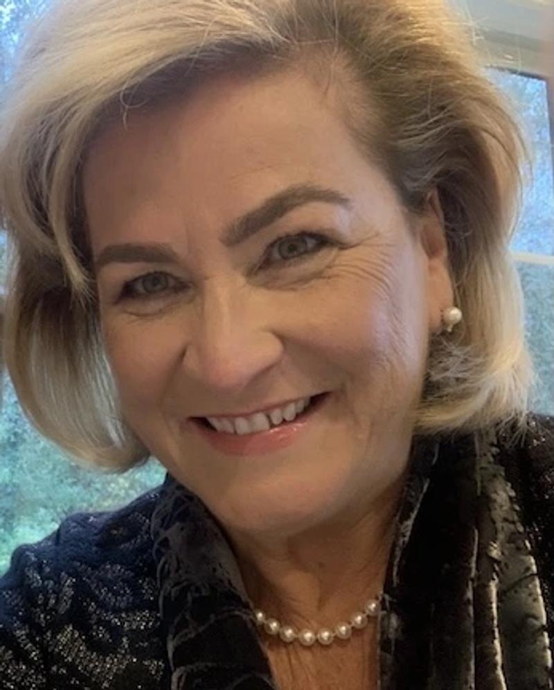 close-up portrait of a smiling woman with blonde bob haircut wearing a pearl necklace and earrings