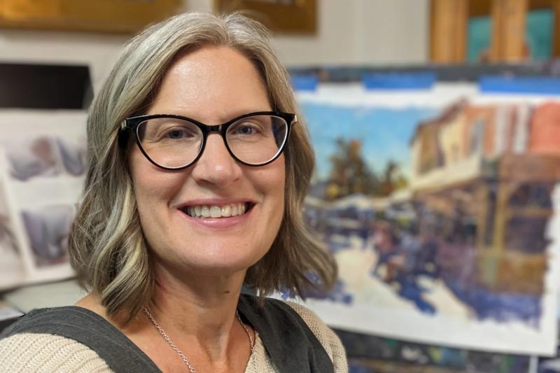smiling woman with glasses in art studio beside painting
