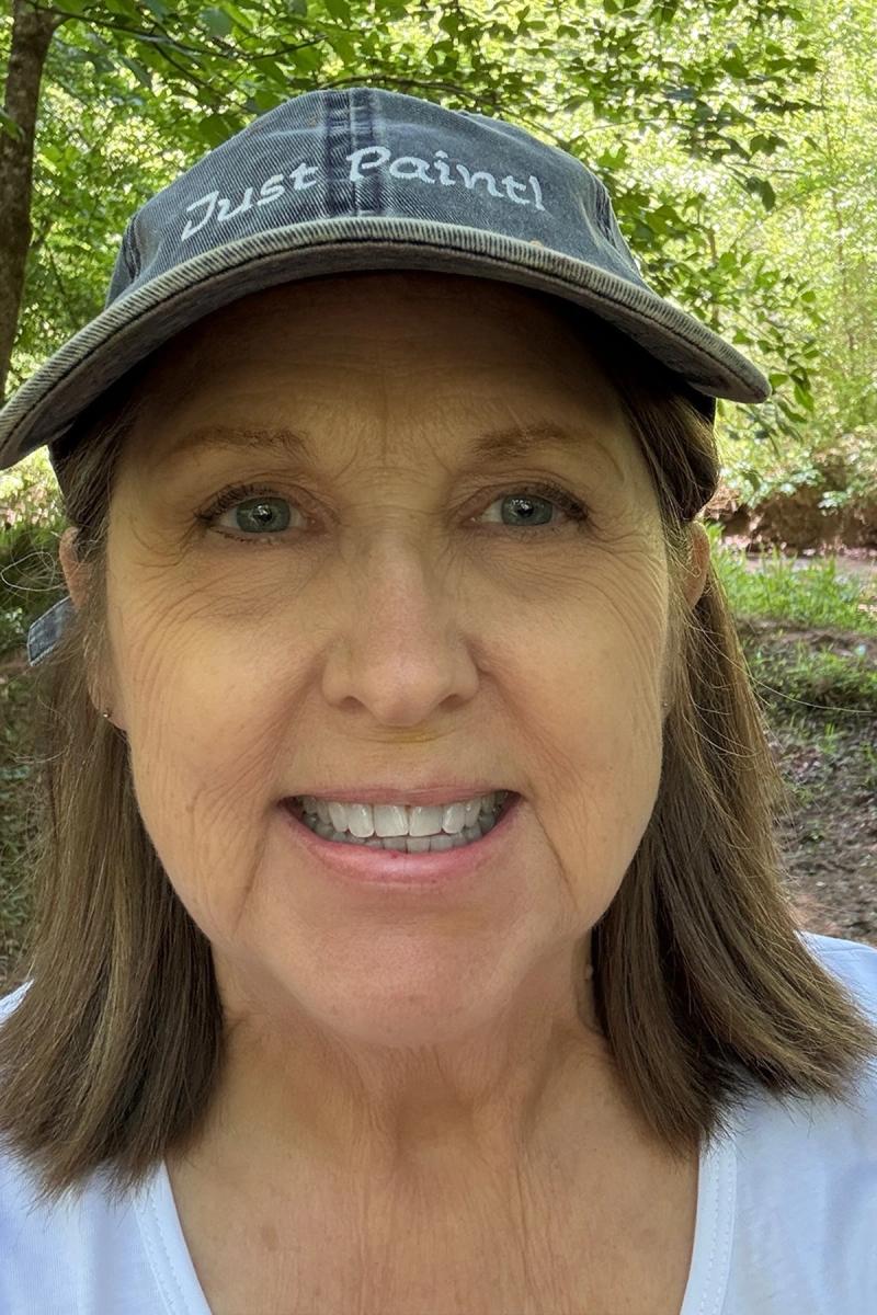 smiling woman in black cap standing in wooded area