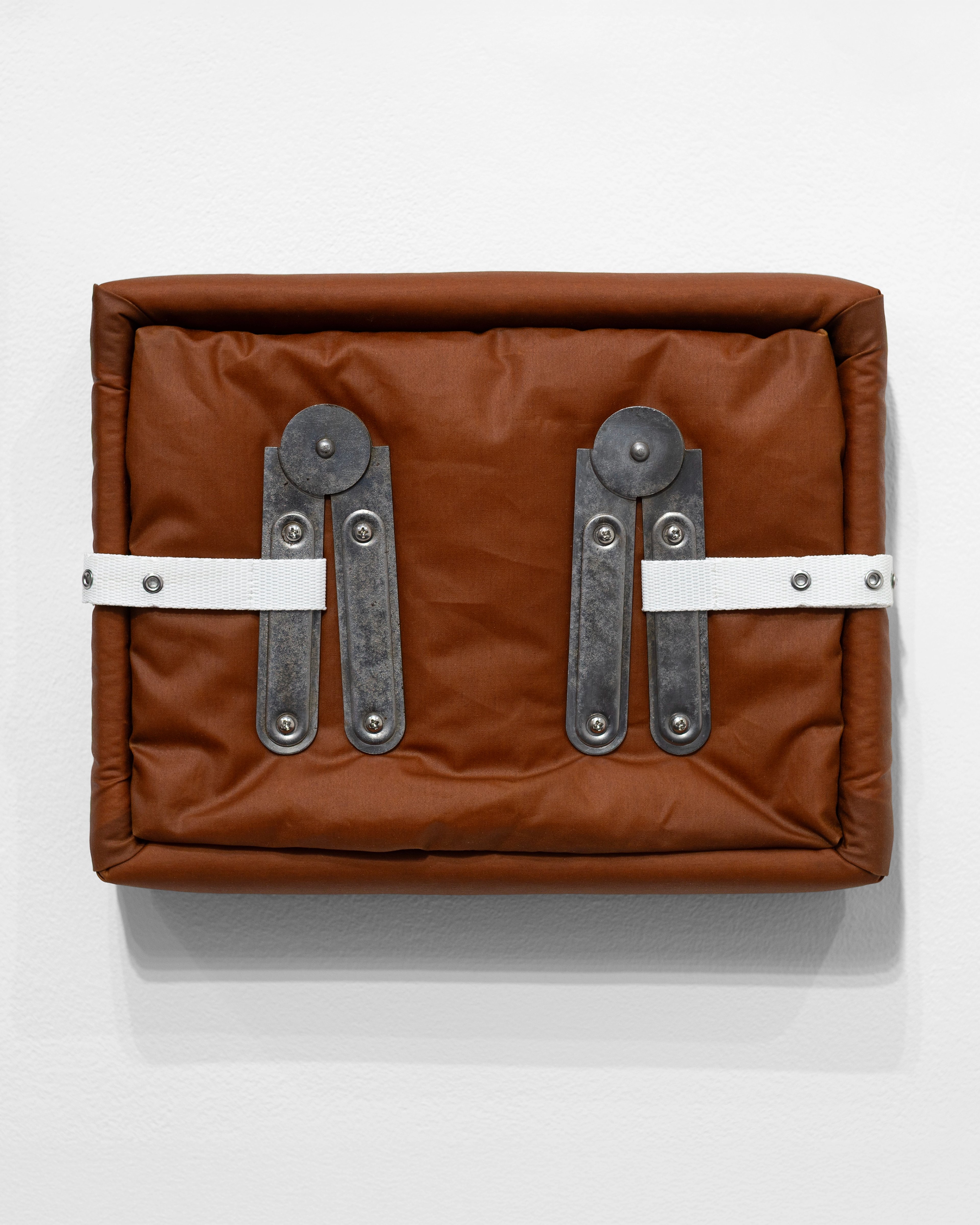 Tan oilskin case with padded edges and white webbing straps fastened by four dark metal toggle hinges with round tops, mounted on white wall
