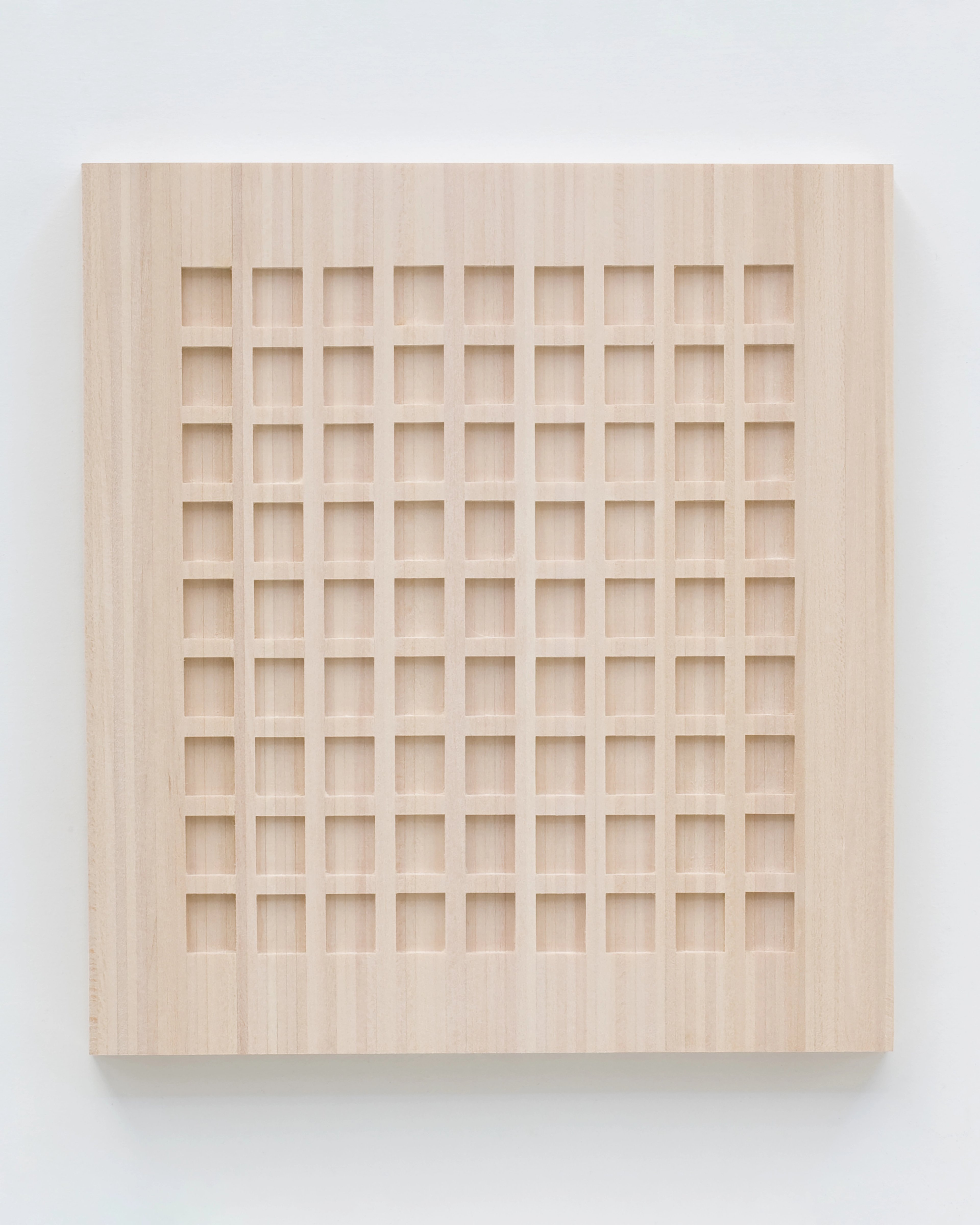 Light wood panel with a grid of 63 shallow rectangular recesses carved in precise rows across the surface