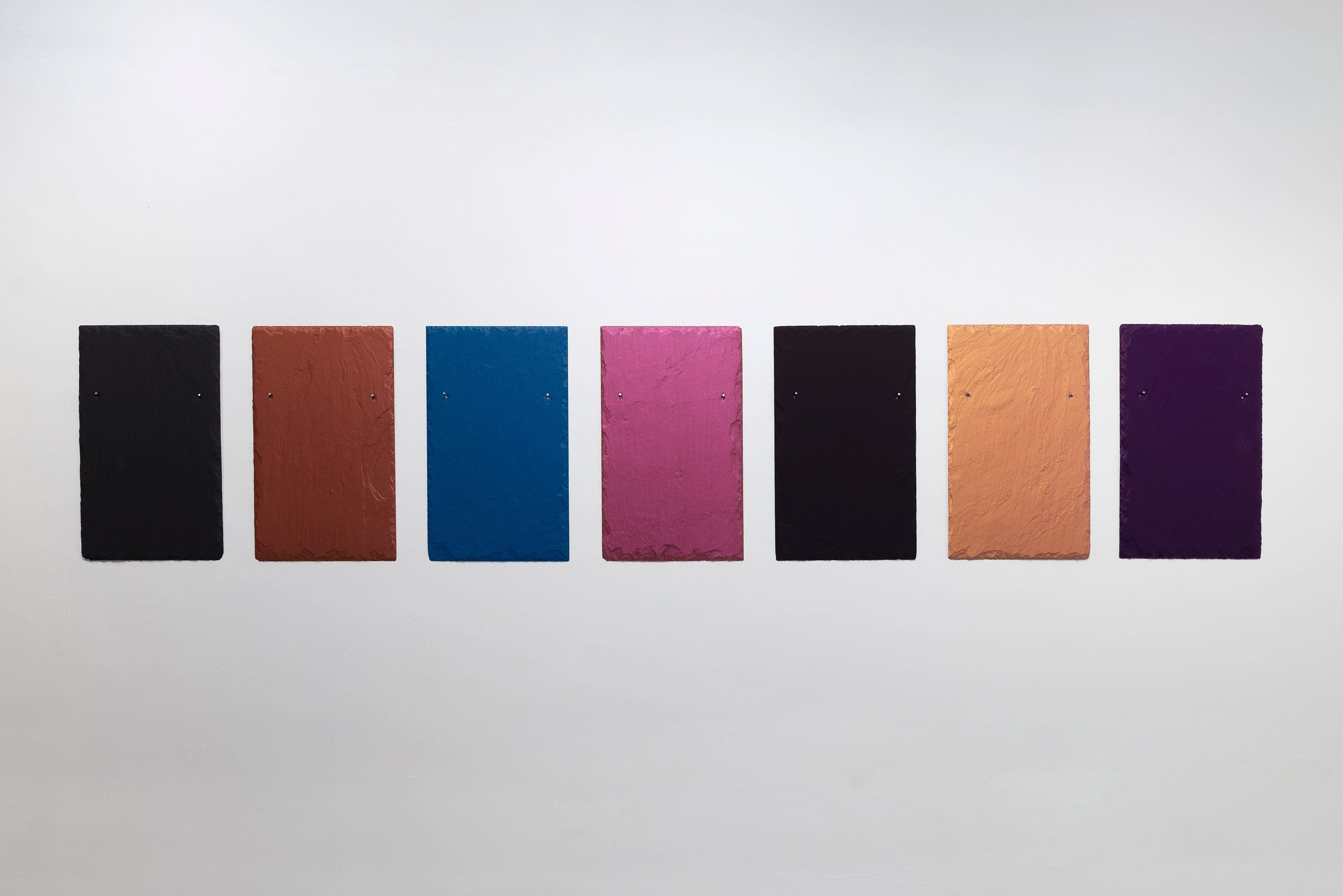 Seven coloured slate panels arranged in a horizontal row: black, terracotta, deep blue, magenta, black, orange, and purple, each with textured surface finish