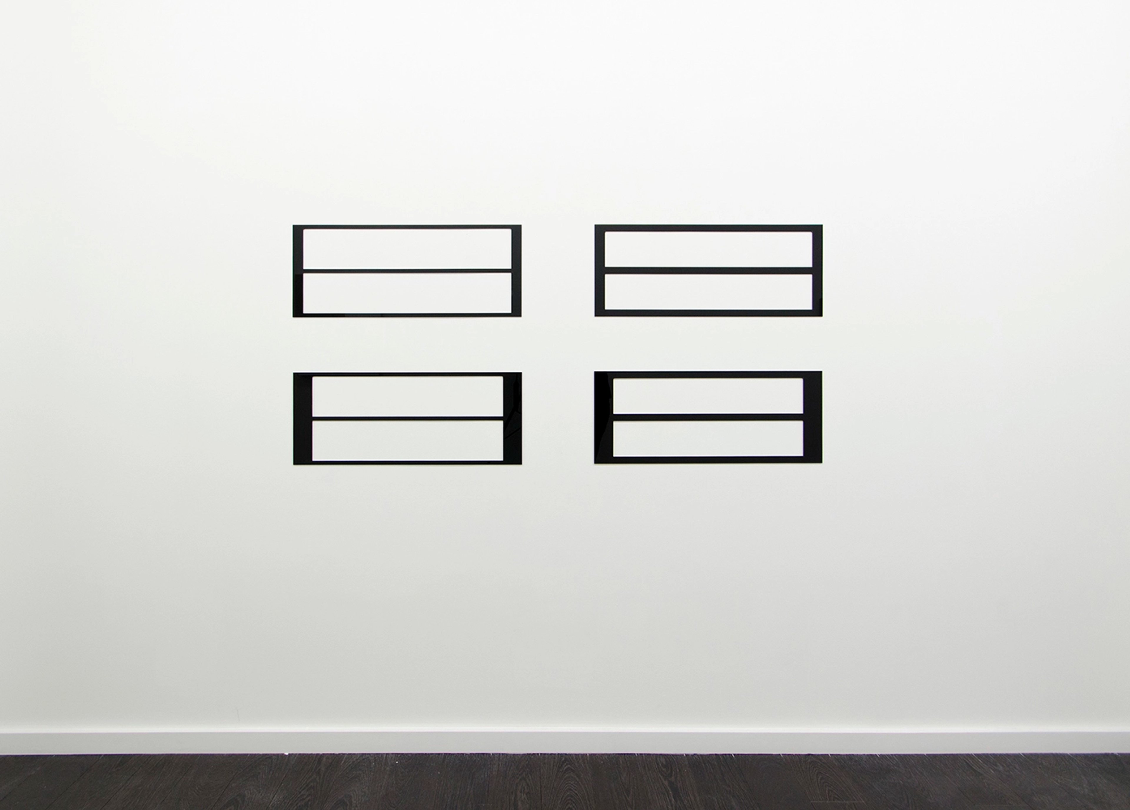 Four black rectangular forms arranged in a 2x2 grid on white wall, each divided horizontally by thin lines, creating a minimal geometric pattern